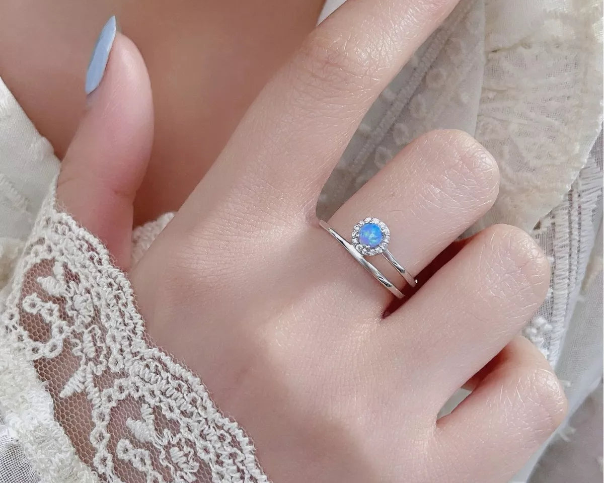 NYLD Glamour Collection by NEWYORKLISTED: Hand wearing a silver ring with a blue gemstone on a lace background