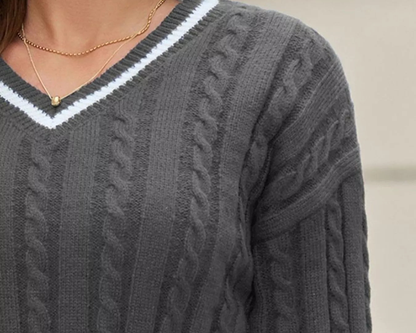 NEWYORKLISTED STYLE COLLECTION: Gray cable knit sweater with a white V-neckline worn by a person.