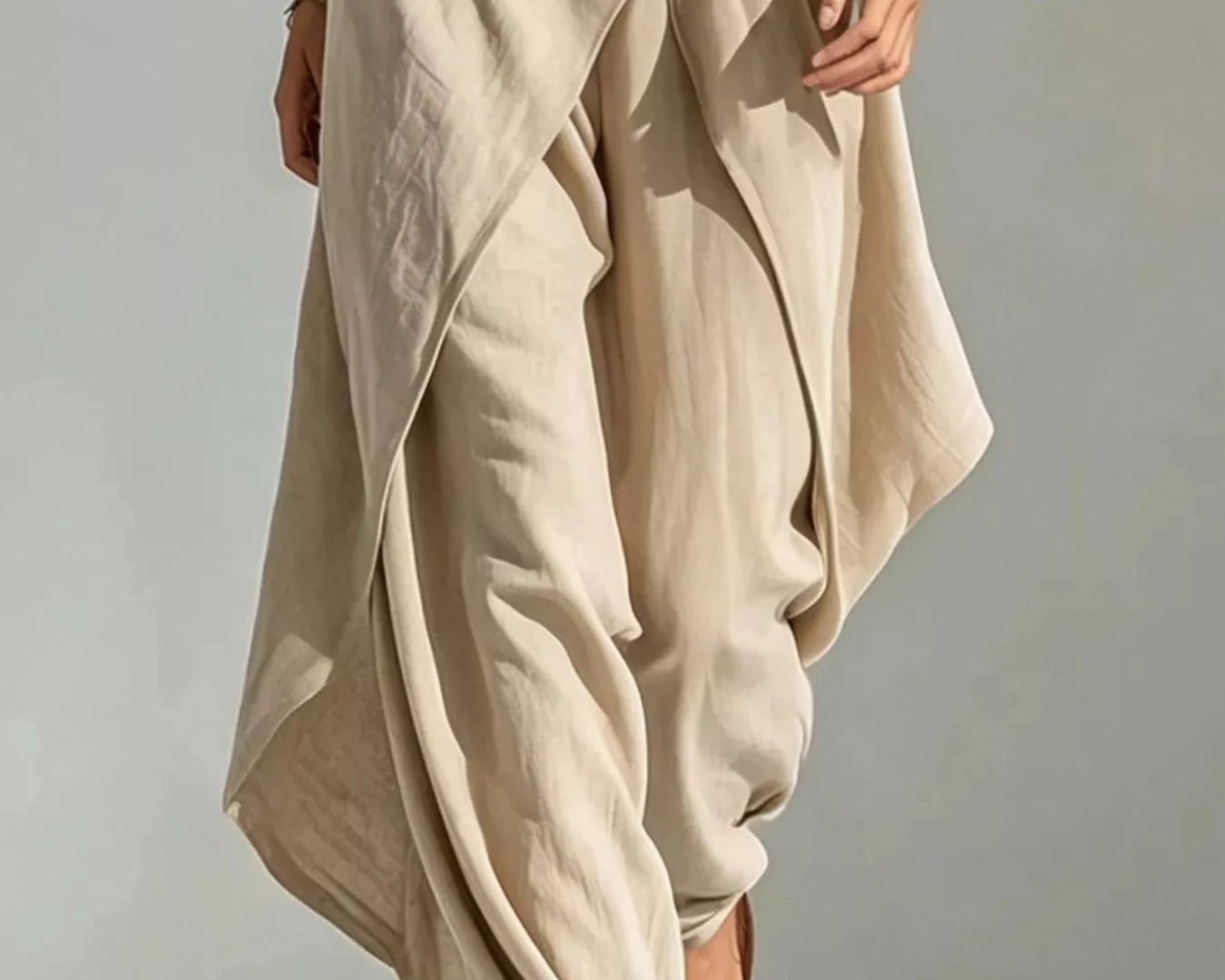 NEWYORKLISTED STYLE COLLECTION: A person wearing loose, draped beige maxi pants with a belted waist, paired with brown slide sandals against a neutral studio background.