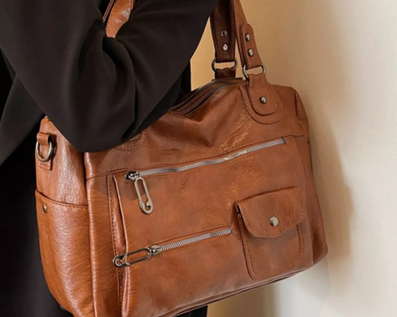 NEWYORKLISTED STYLE COLLECTION: Brown leather handbag held by a person against a neutral background