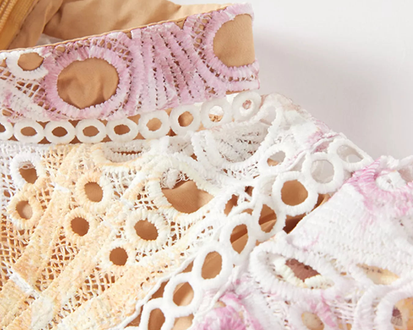 NEWYORKLISTED STYLE COLLECTION: Close-up of pink, white, and beige lace fabric on a wooden surface.