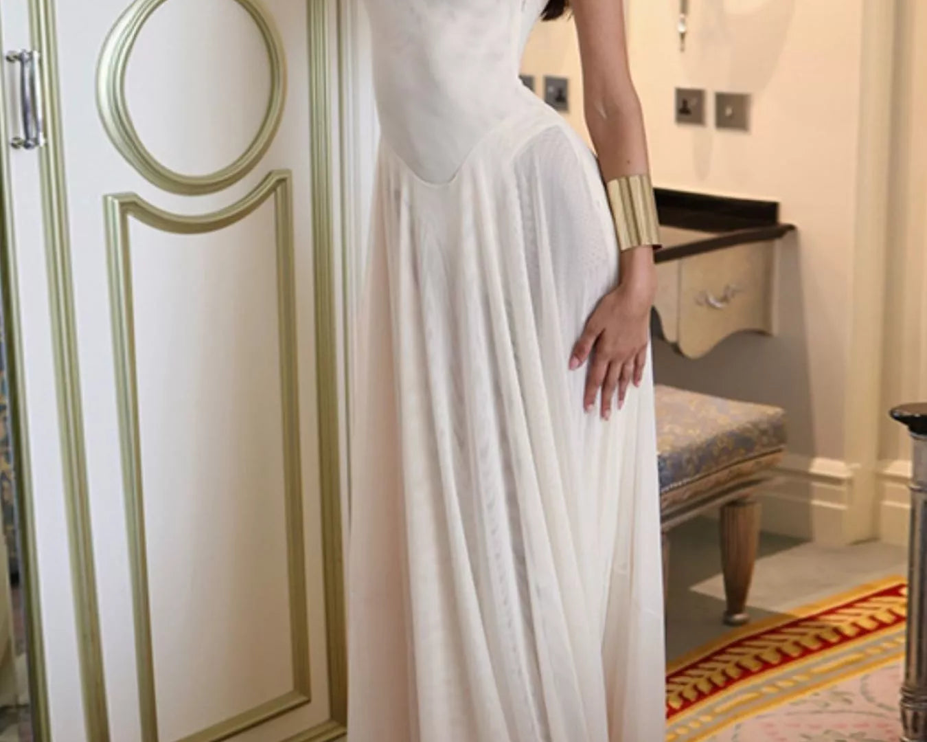 NEWYORKLISTED STYLE COLLECTION: Woman in a white evening gown standing in an elegant room with decorative walls.