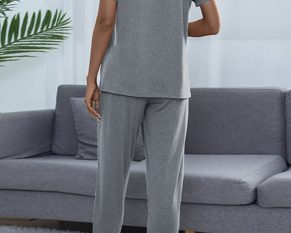 Person wearing gray pajamas standing in a living room with a gray sofa and white curtains.