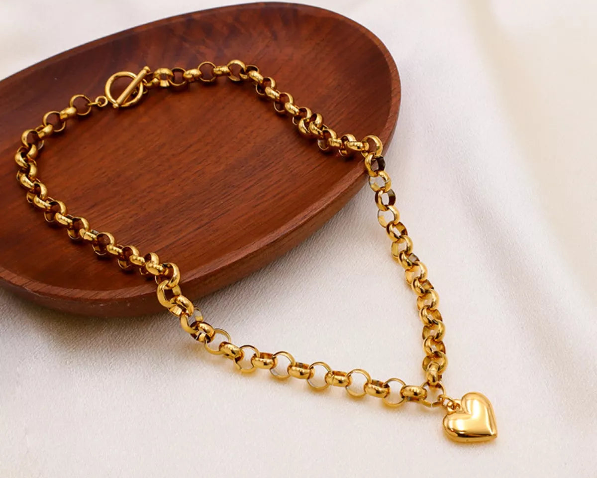 NYLD Glamour Collection by NEWYORKLISTED: Gold chain bracelet with a heart charm on a wooden tray