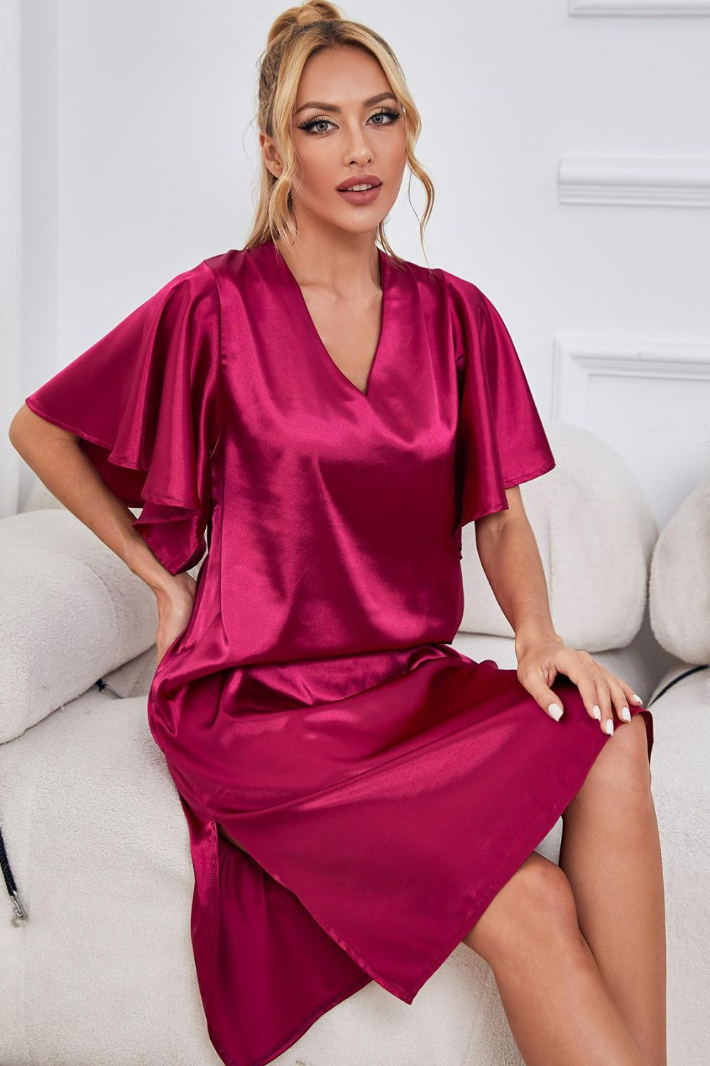 NEWYORKLISTED Intimate Apparel: Woman wearing a vibrant pink satin dress sitting on a white couch.