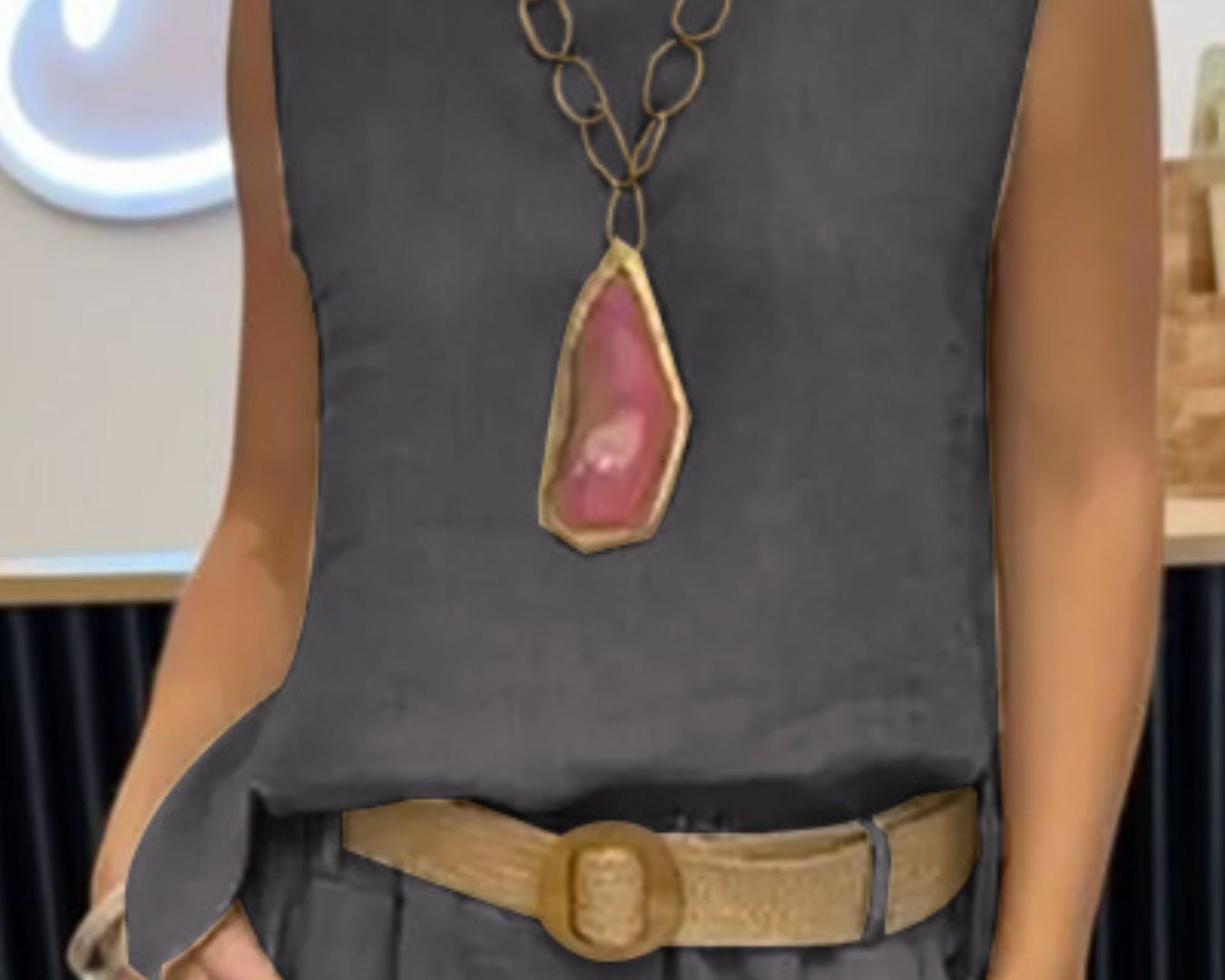 NEWYORKLISTED COMFORT COLLECTION: Person wearing a gray sleeveless top with a large necklace and belt, standing indoors.