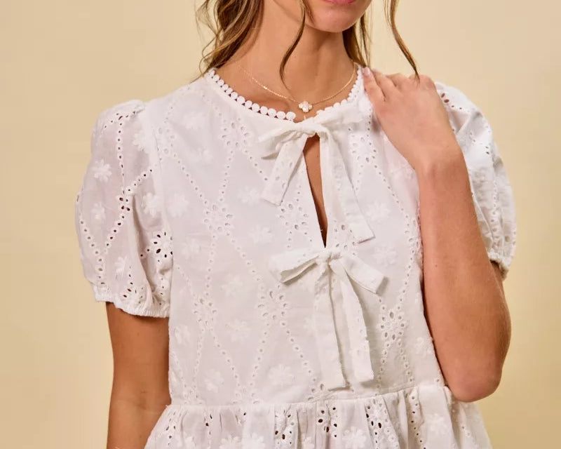NEWYORKLISTED STYLE COLLECTION: Woman wearing a white lace top with puffed sleeves against a beige background