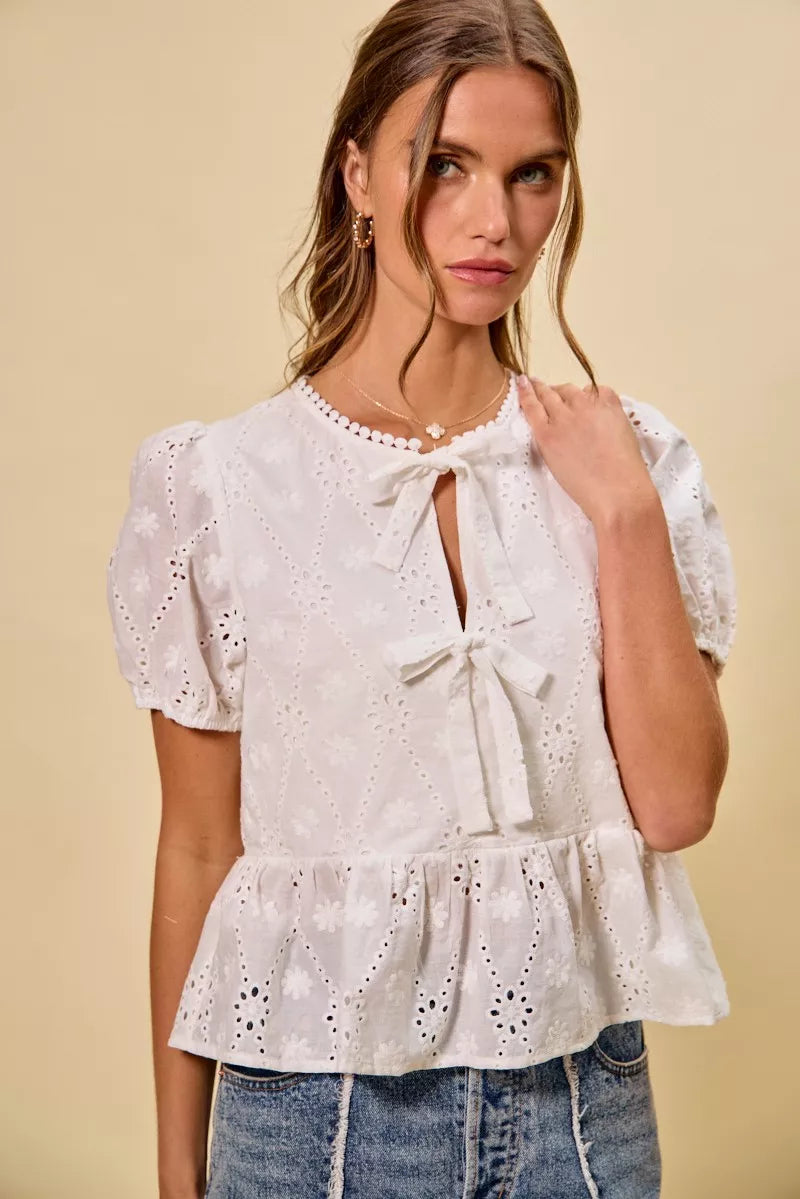NEWYORKLISTED STYLE COLLECTION: Woman wearing a white lace top with puffed sleeves against a beige background