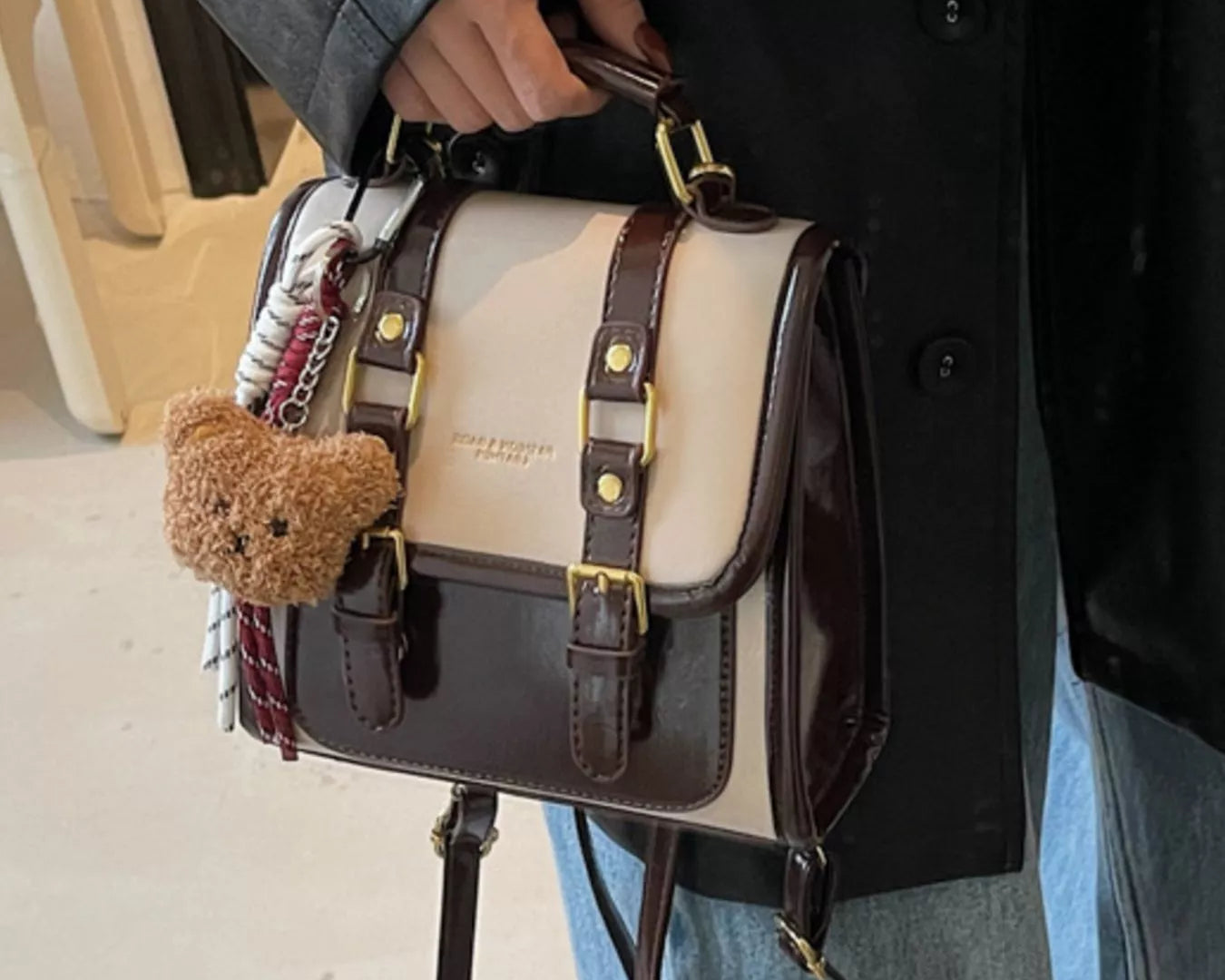 NEWYORKLISTED STYLE COLLECTION: Person holding a black and beige handbag with a teddy bear charm.