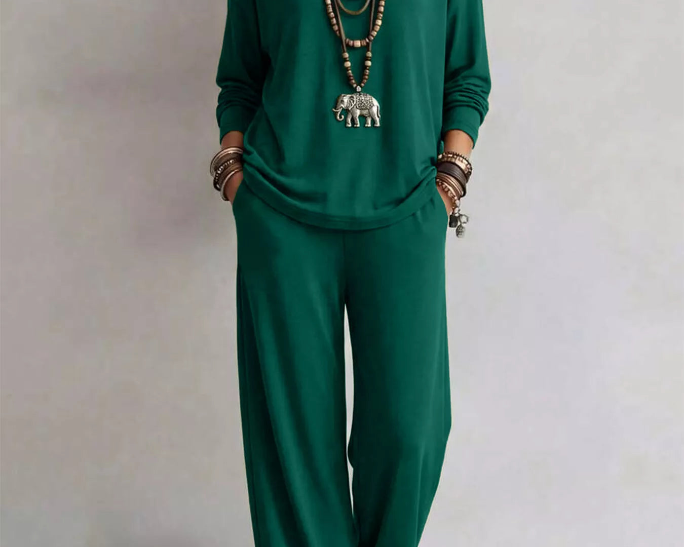 NEWYORKLISTED STYLE COLLECTION: A woman modeling a matching dark green long-sleeve top and wide-leg pants set, accessorized with layered necklaces, bracelets, and sandals, against a plain light gray background.