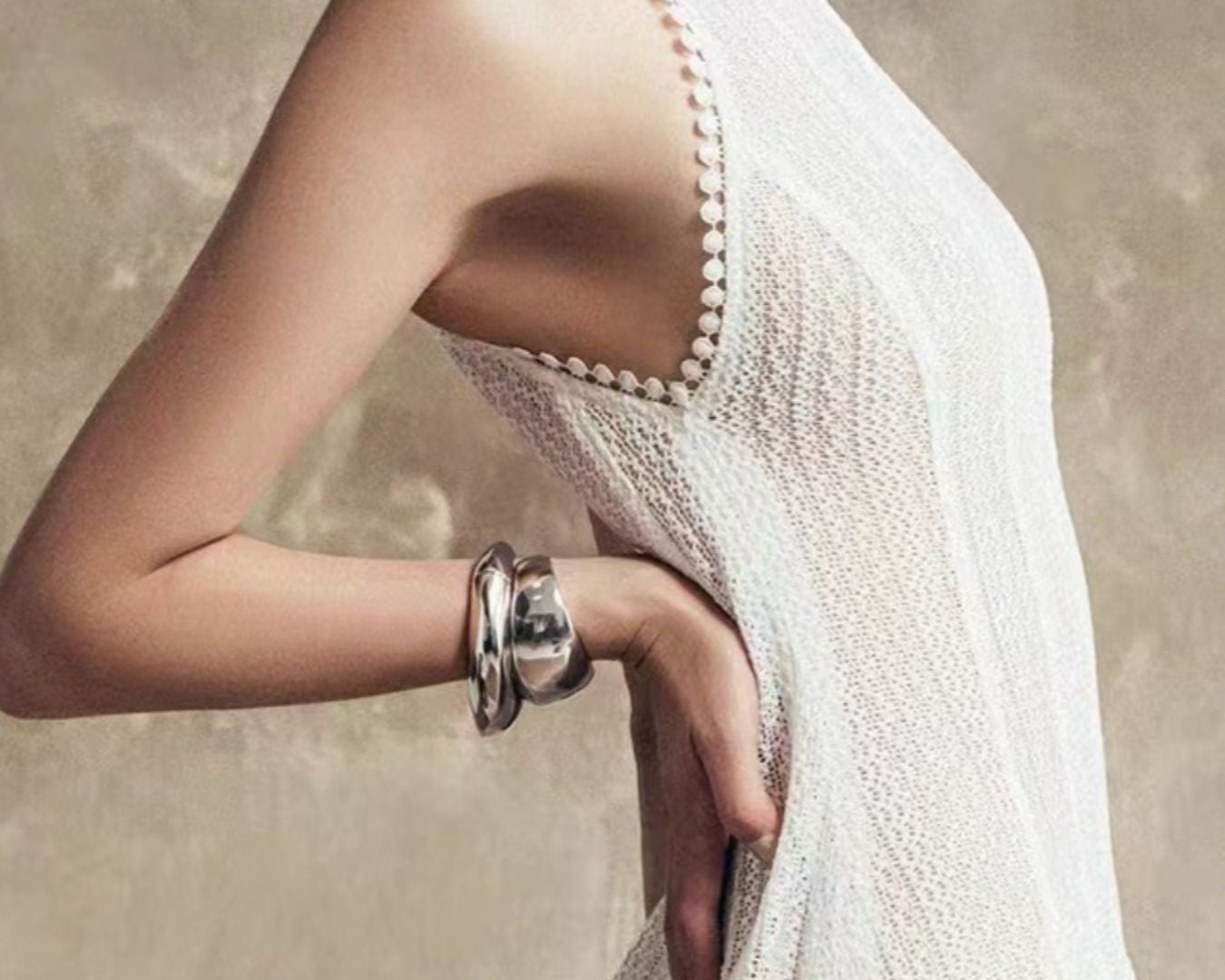NEWYORKLISTED STYLE COLLECTION: Woman wearing a white dress with a textured back design, holding her arm with a bracelet.