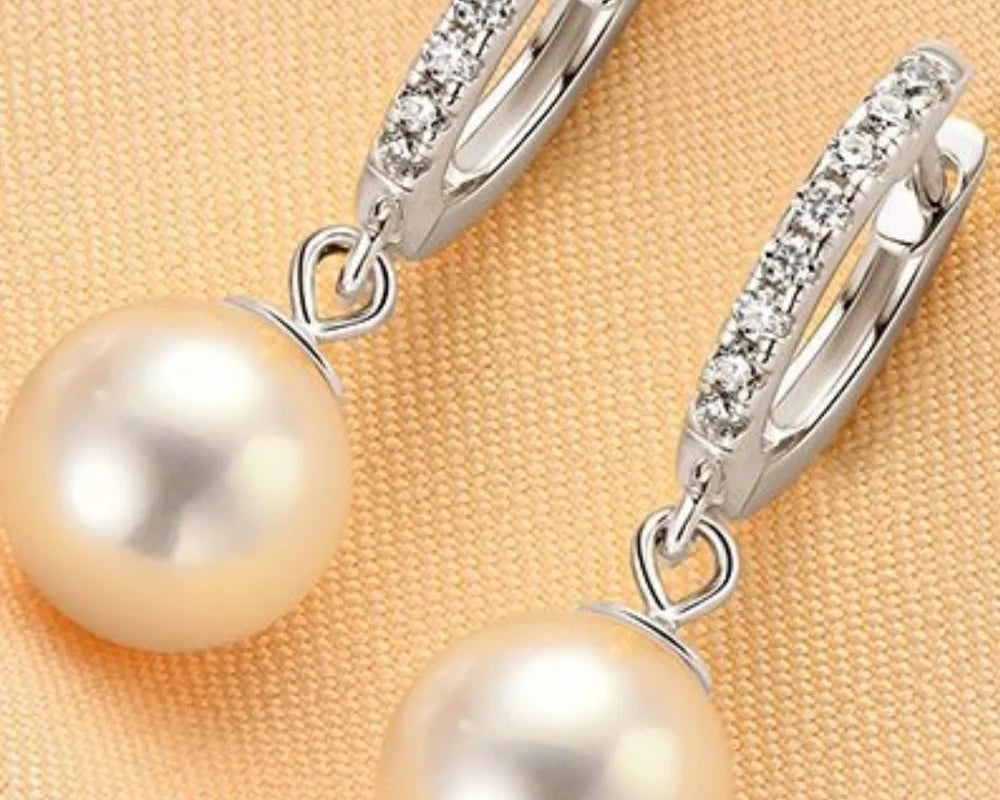 NYLD GLAMOUR COLLECTION by NEWYORKLISTED: Pearl earrings with silver hooks on a beige fabric background