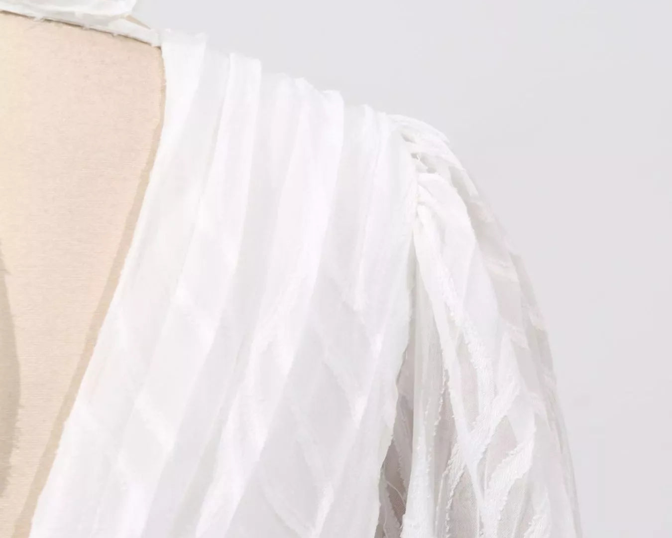 NEWYORKLISTED STYLE COLLECTION: White dress with a sheer overlay on a mannequin against a light gray background
