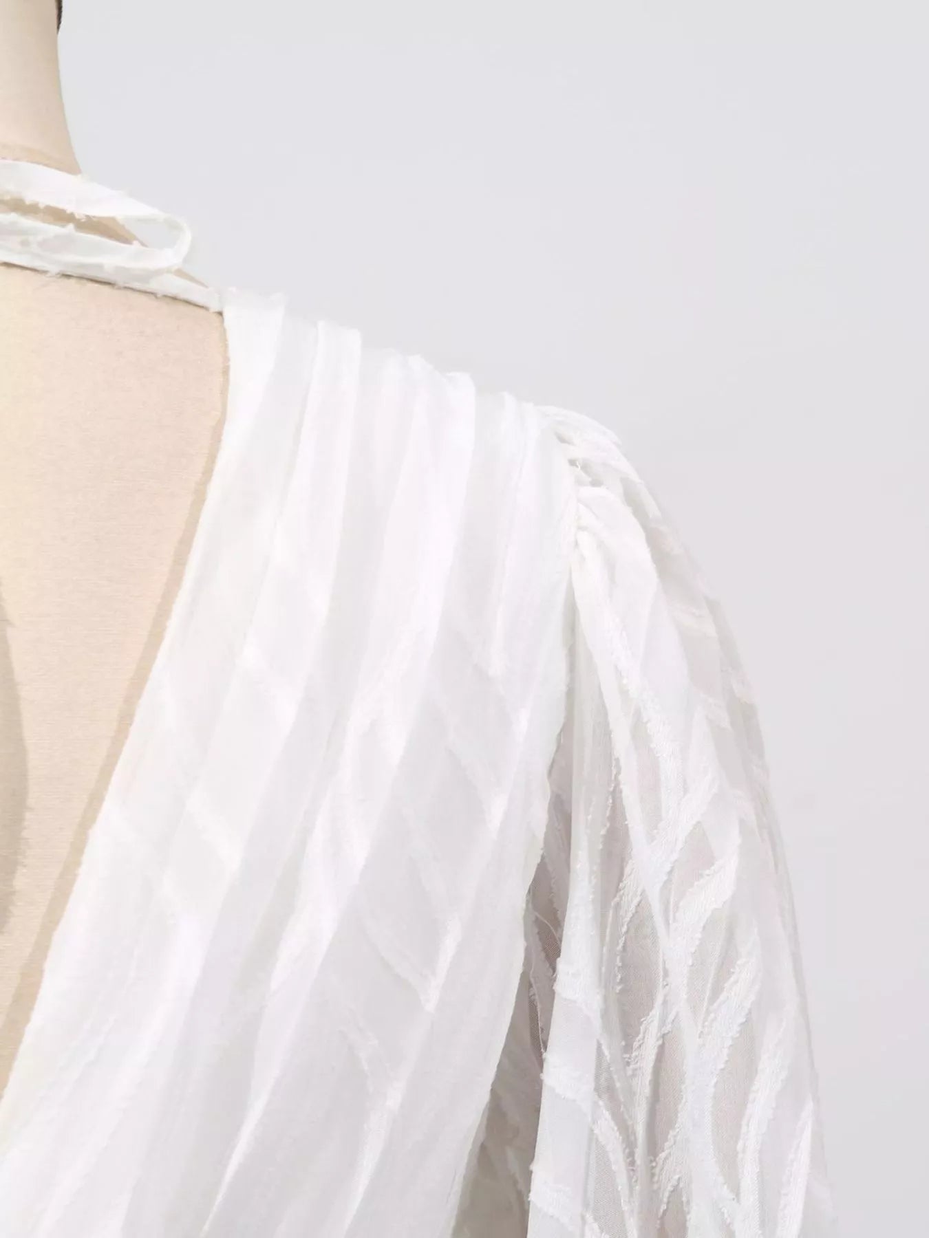 NEWYORKLISTED STYLE COLLECTION: White dress with a sheer overlay on a mannequin against a light gray background