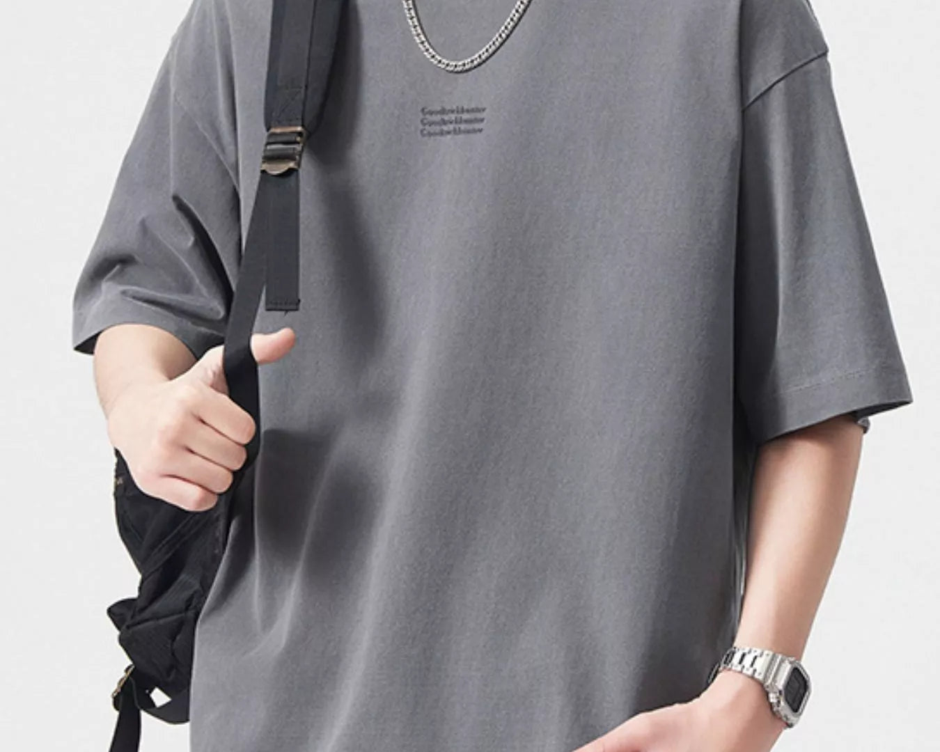NEWYORKLISTED ATLAS MEN's COLLECTION: Person wearing a gray t-shirt with a small logo, holding a black backpack on a light gray background