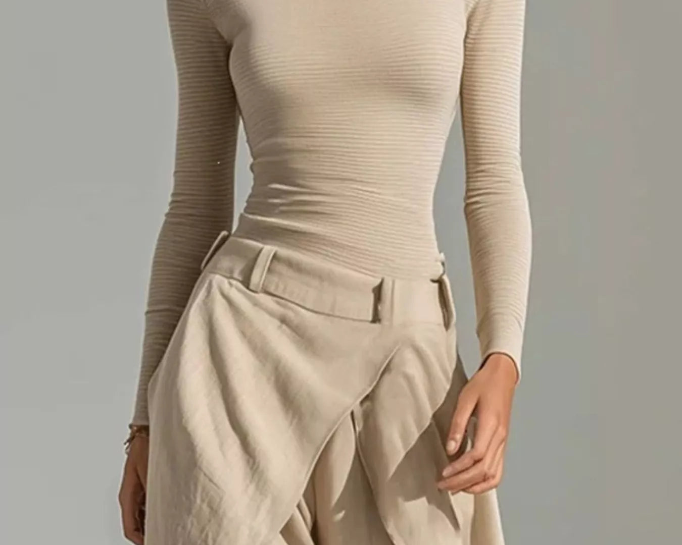 NEWYORKLISTED STYLE COLLECTION: A woman wearing a beige off-the-shoulder long-sleeve ribbed top and matching draped high-waisted trousers, photographed against a plain light gray studio background.