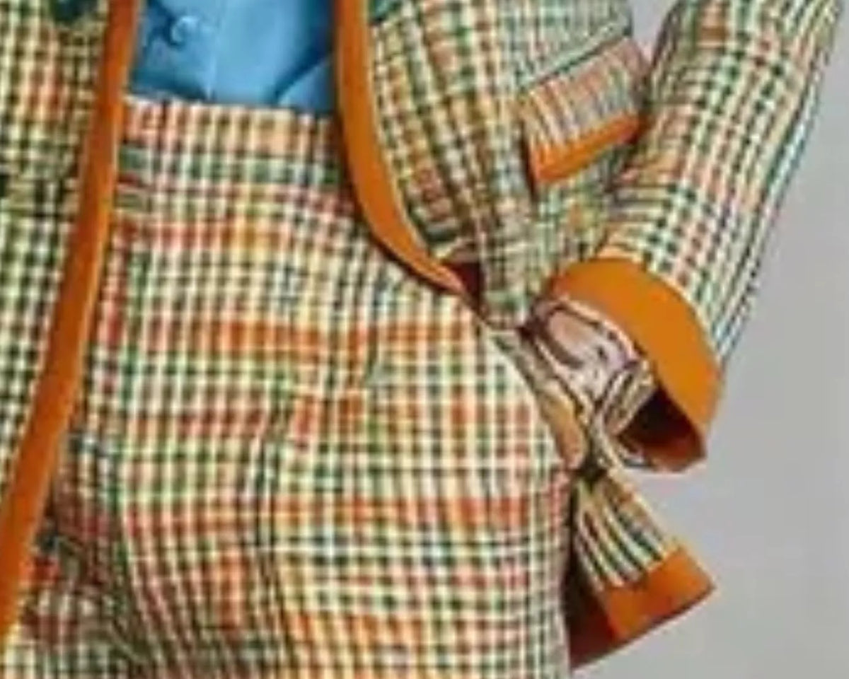NEWYORKLISTED STYLE COLLECTION: A close-up of a men's plaid suit jacket and matching trousers with orange-brown trim, worn over a light blue button-up shirt.