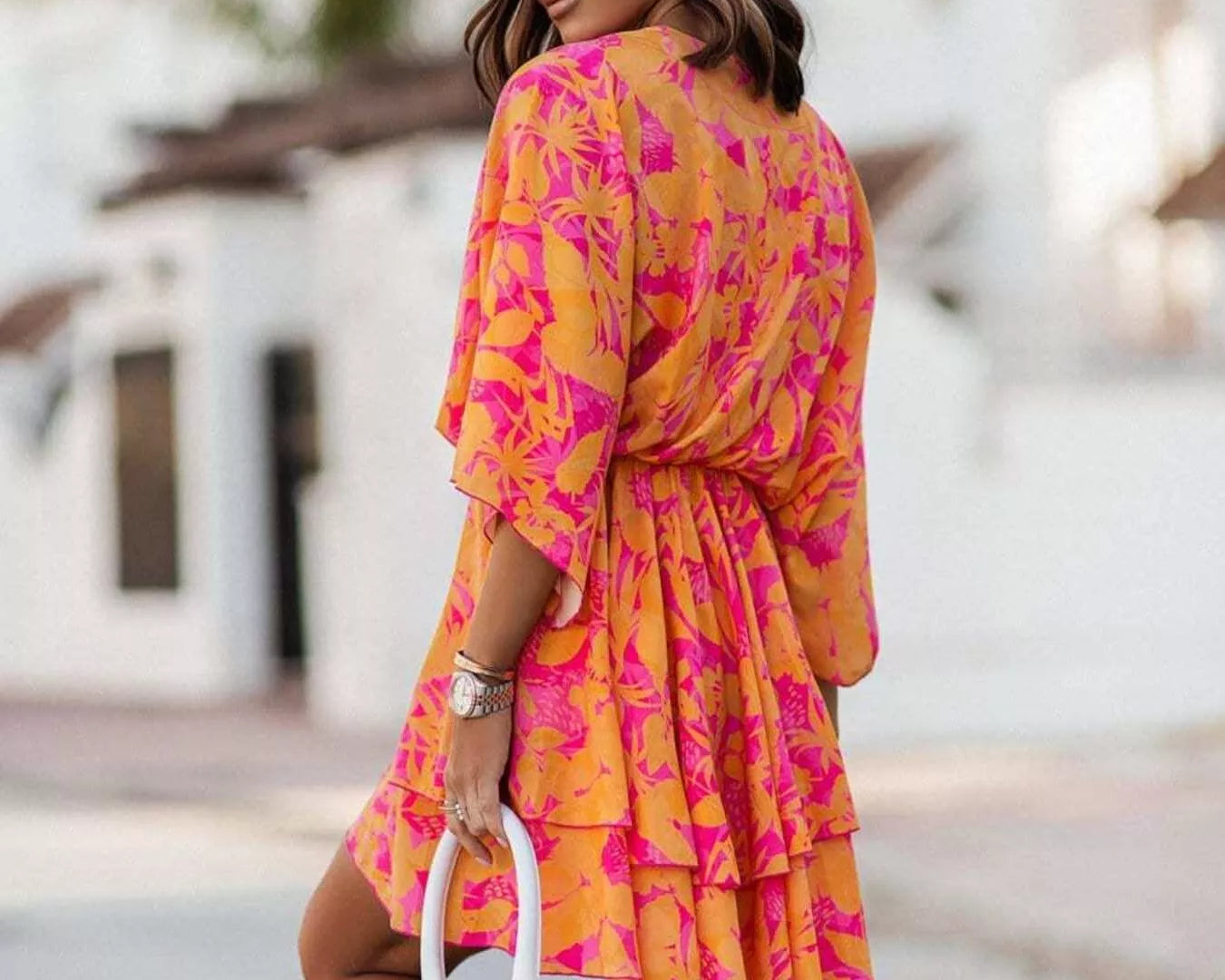 NEWYORKLISTED STYLE COLLECTION: Woman wearing a vibrant pink and orange dress with a blurred outdoor background