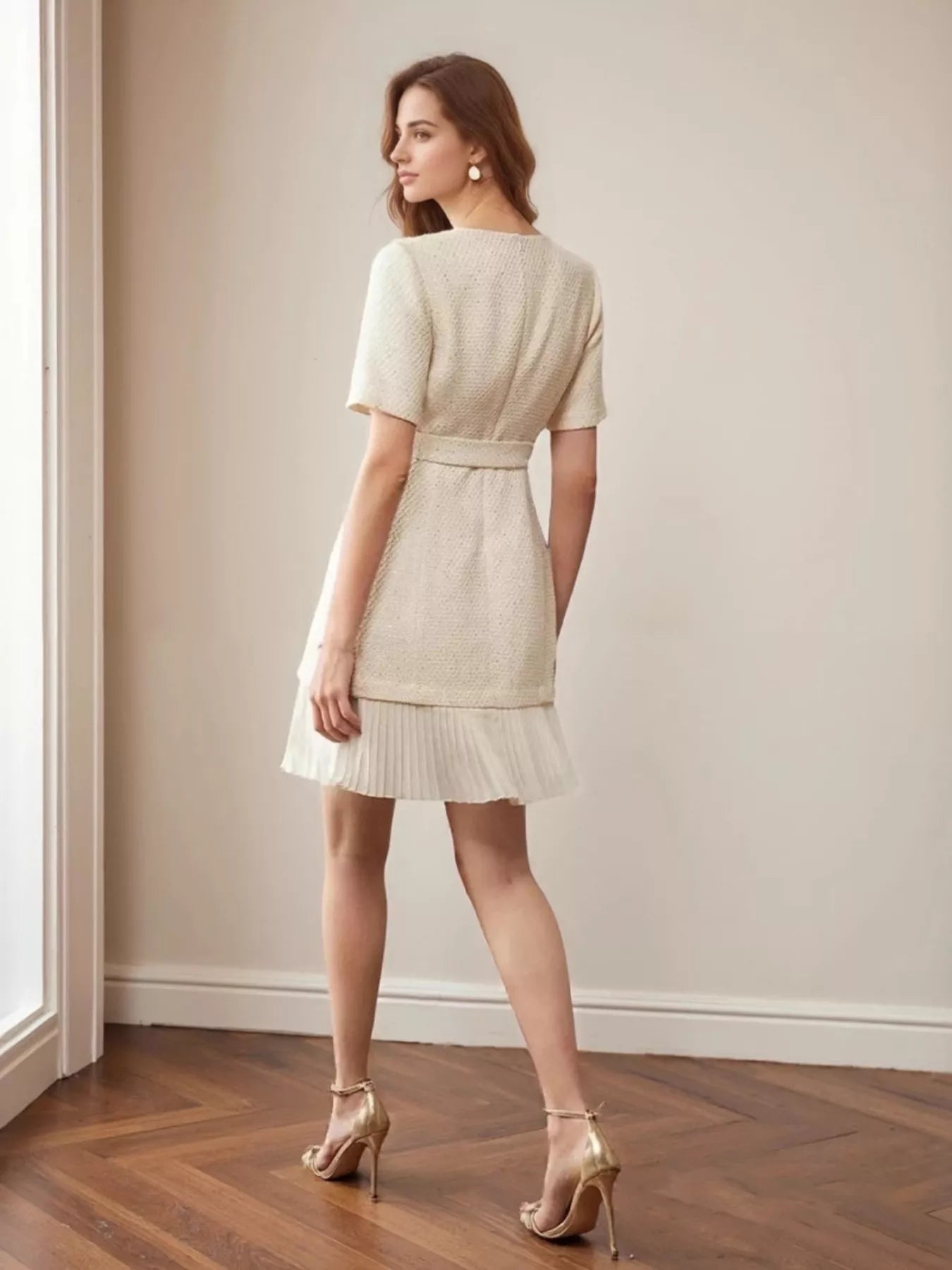 NEWYORKLISTED STYLE COLLECTION: Model wearing a beige dress standing in a room with wooden flooring and a neutral wall.