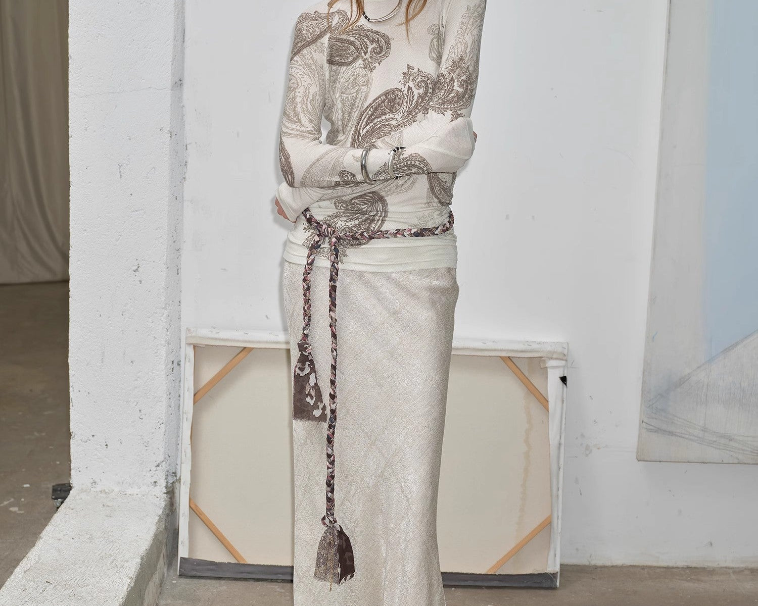 NEWYORKLISTED STYLE COLLECTION: Woman wearing a long, light-colored dress with intricate patterns in a minimalistic setting.