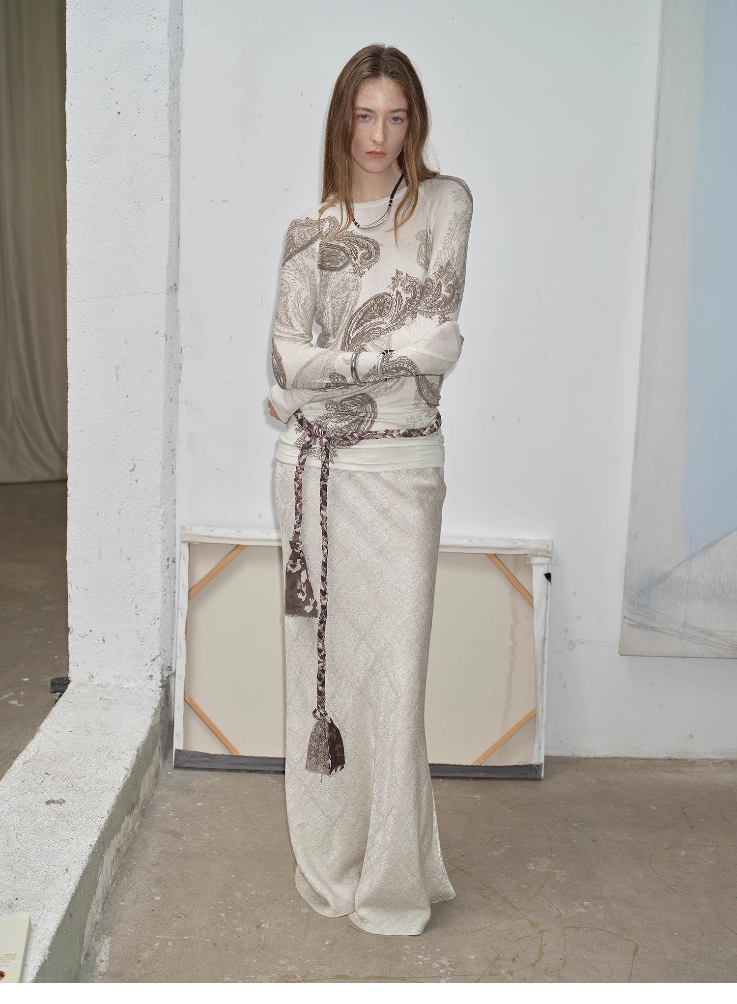 NEWYORKLISTED STYLE COLLECTION: Woman wearing a long, light-colored dress with intricate patterns in a minimalistic setting.