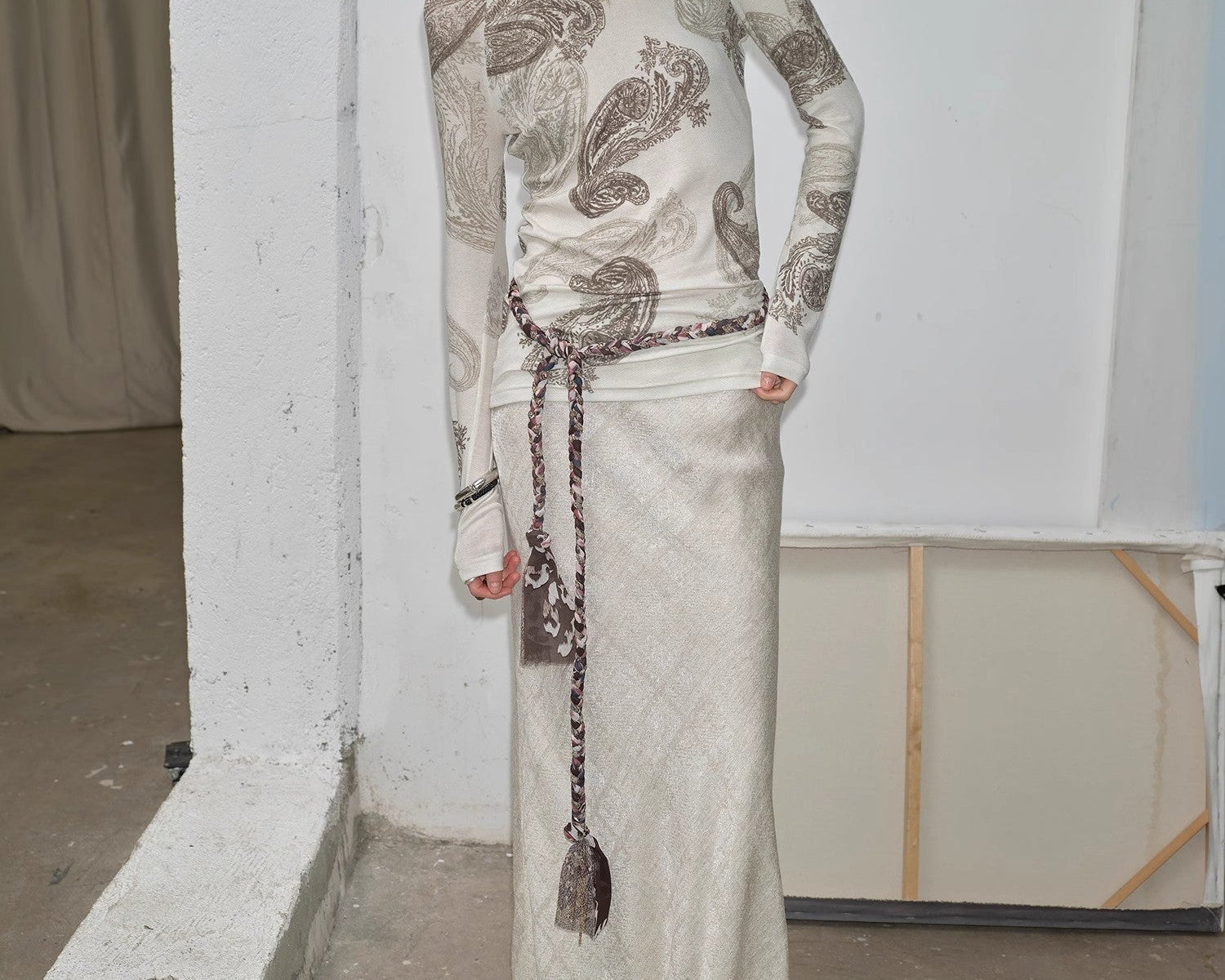 Woman wearing a long, patterned dress against a plain wall.