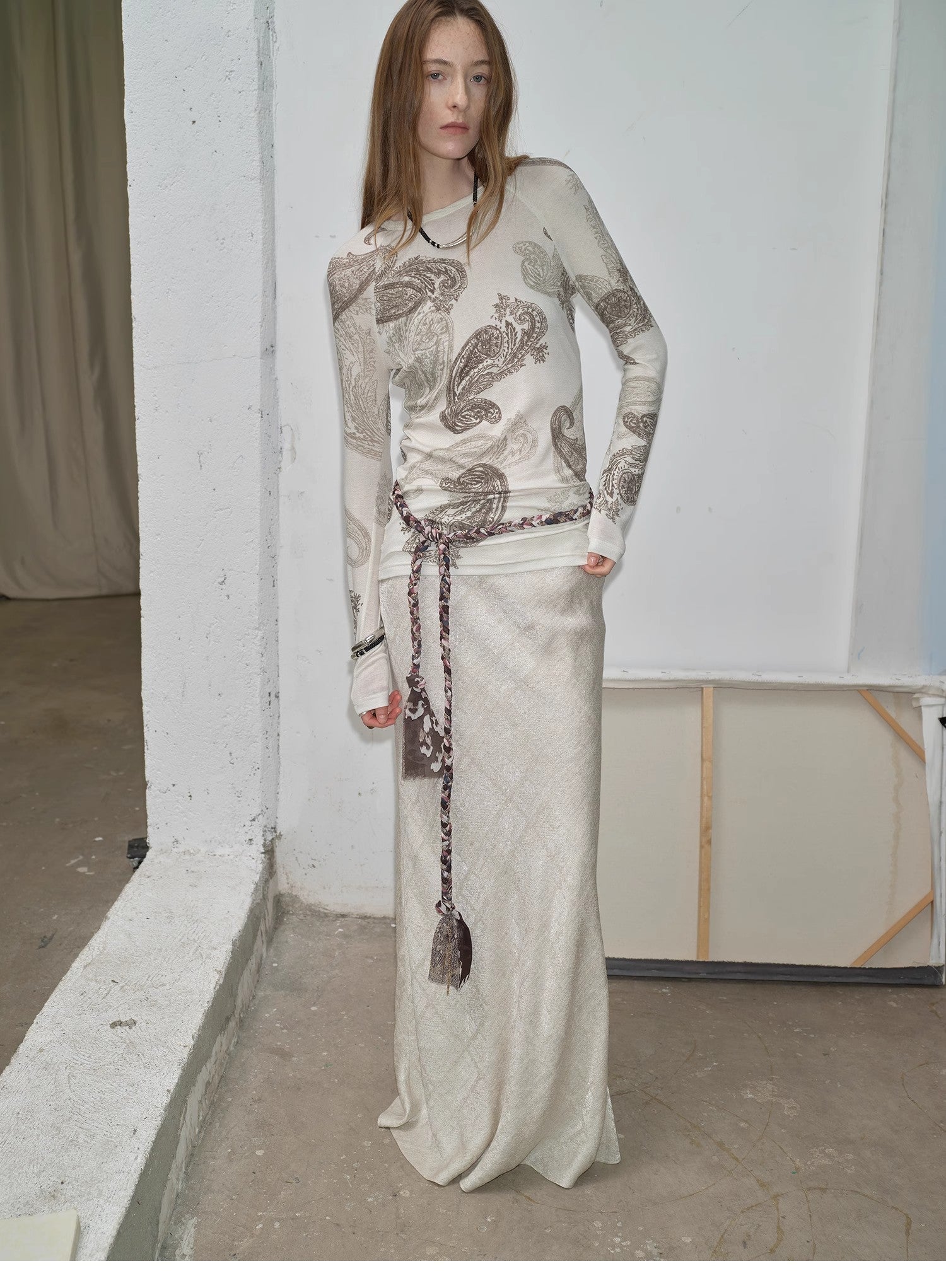 Woman wearing a long, patterned dress against a plain wall.