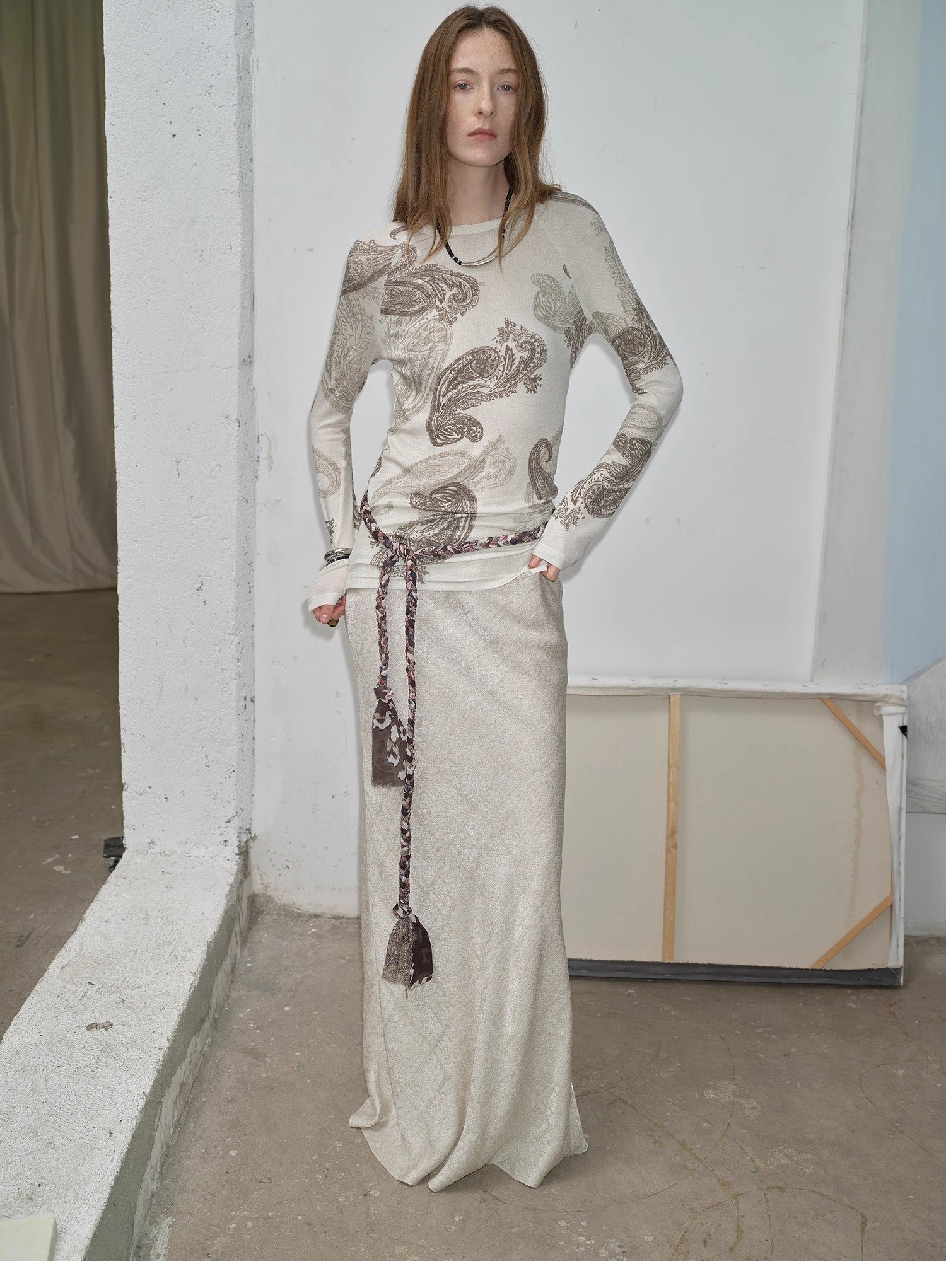 NEWYORKLISTED STYLE COLLECTION: Woman wearing a long, patterned dress standing against a plain wall.