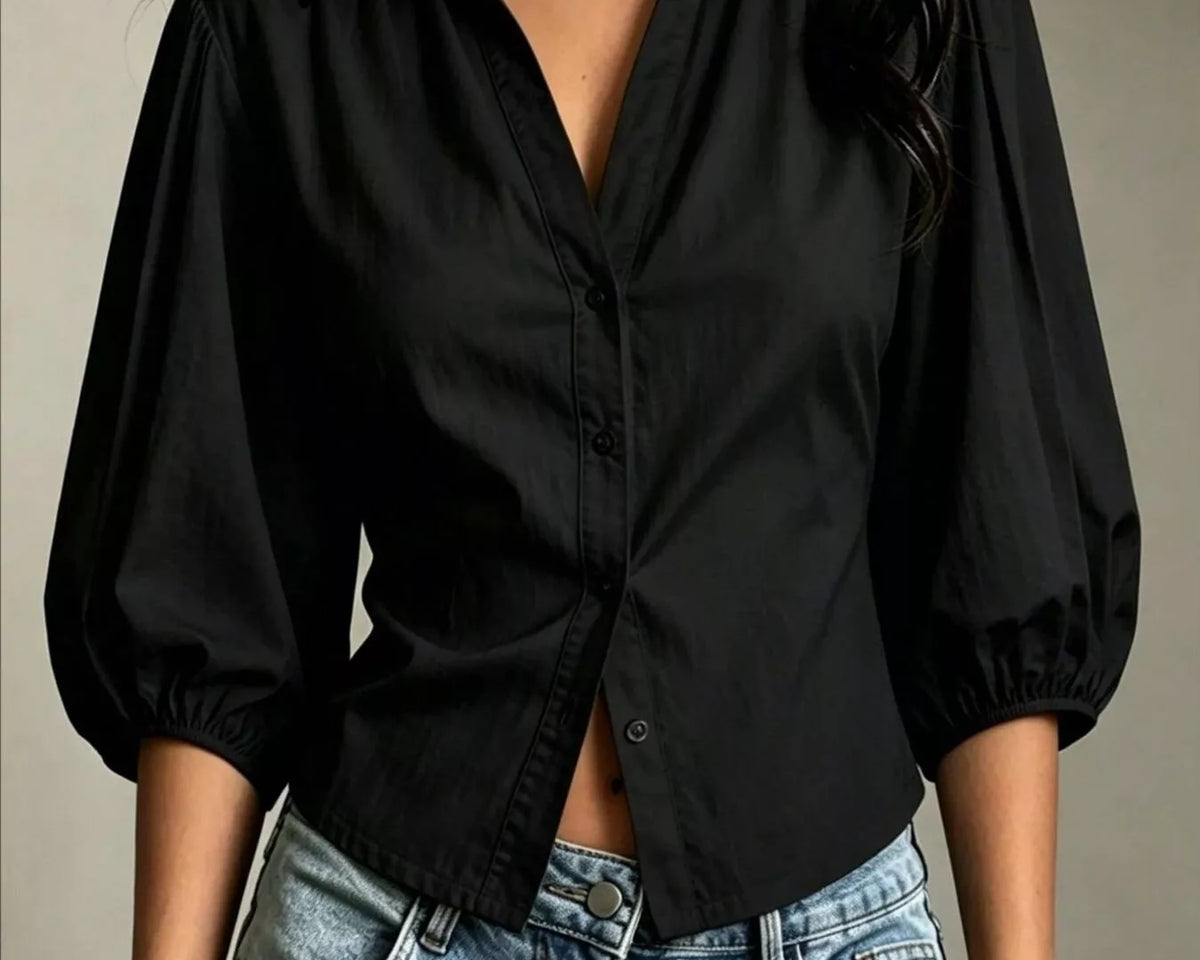 NEWYORKLISTED STYLE COLLECTION: A woman wearing a black long-sleeve button-up blouse with voluminous puff sleeves and light-wash blue jeans, shown from the neck down against a neutral indoor wall.