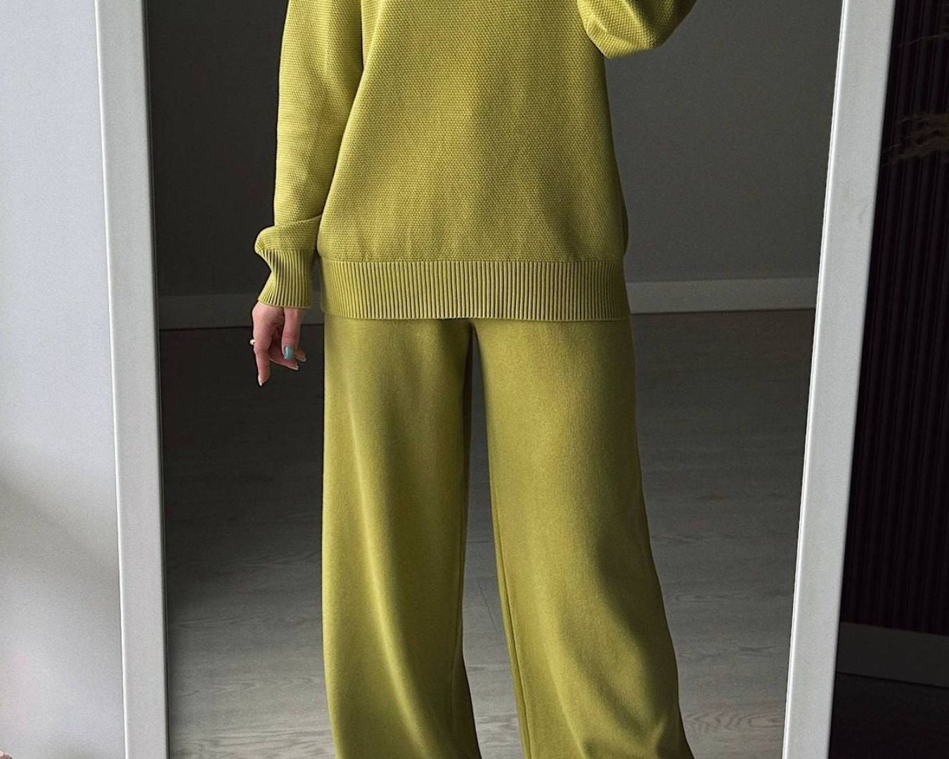Person wearing a green sweater and pants standing in front of a mirror.
