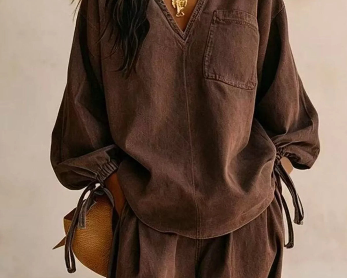 NEWYORKLISTED STYLE COLLECTION: A woman wearing a loose brown long-sleeve top and matching wide-leg pants, styled with a gold necklace, blue earrings, and a brown woven bag against a neutral beige background.