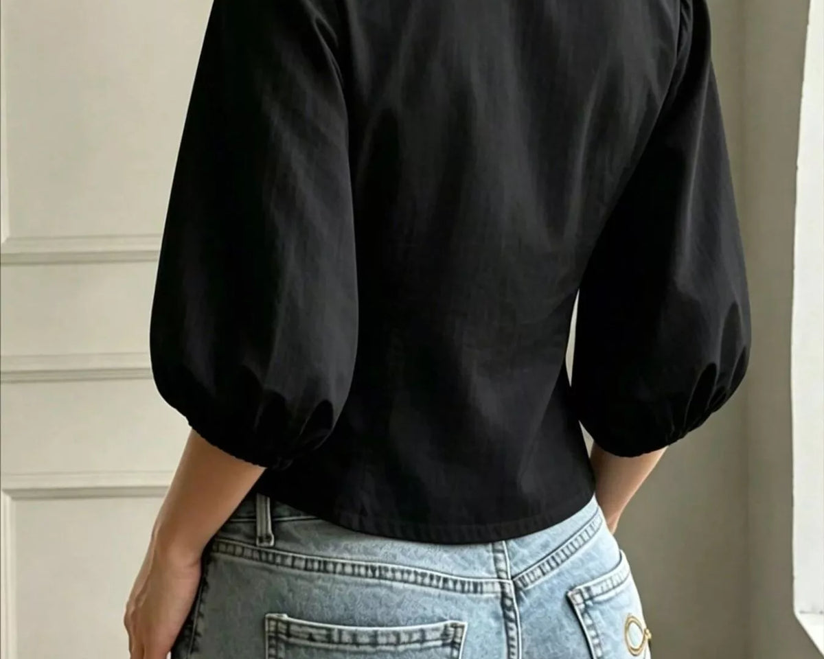 NEWYORKLISTED STYLE COLLECTION: A woman shown from the back wearing a black puff-sleeve collared blouse tucked into light-wash blue jeans with decorative bow embroidery on the back pockets.