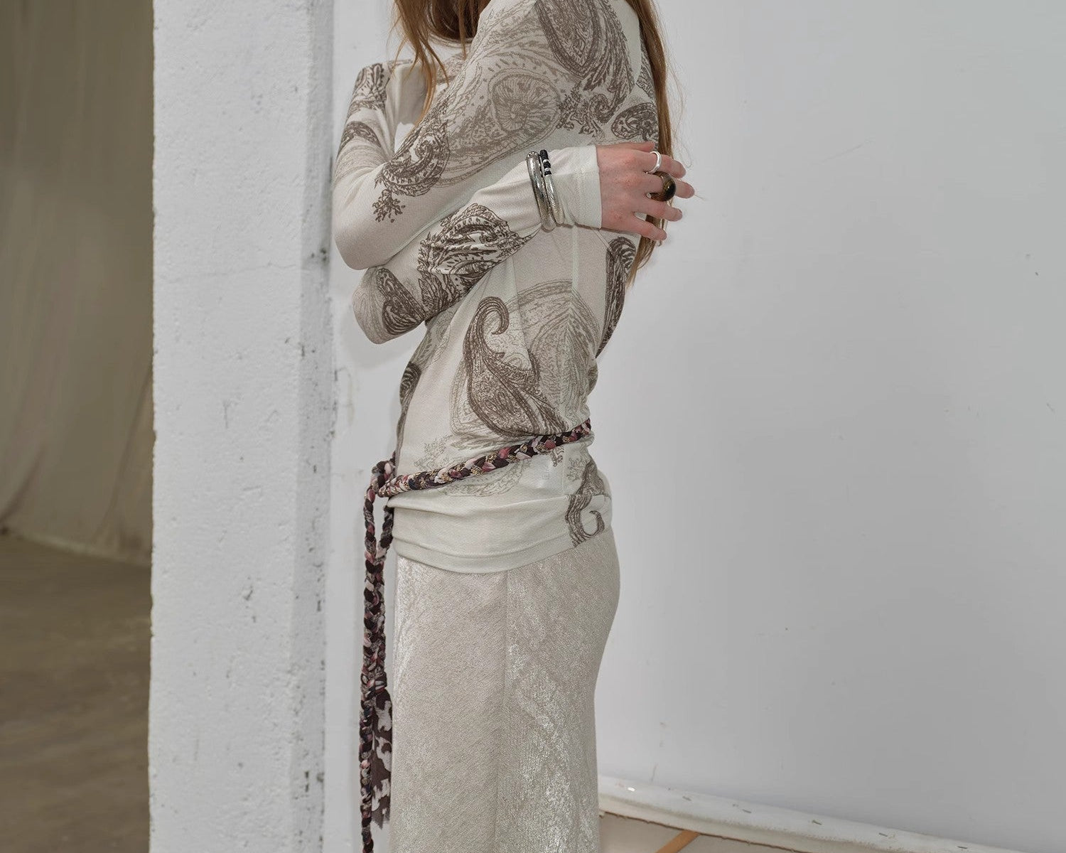 Woman wearing a patterned top and skirt standing against a white wall.