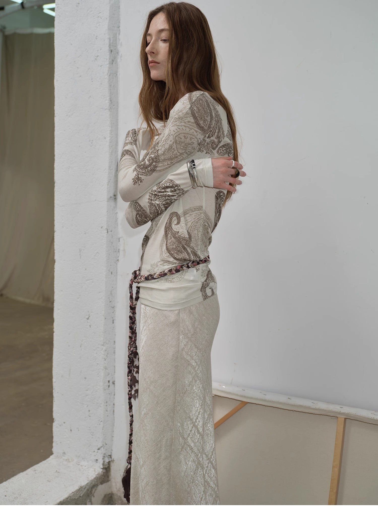 Woman wearing a patterned top and skirt standing against a white wall.