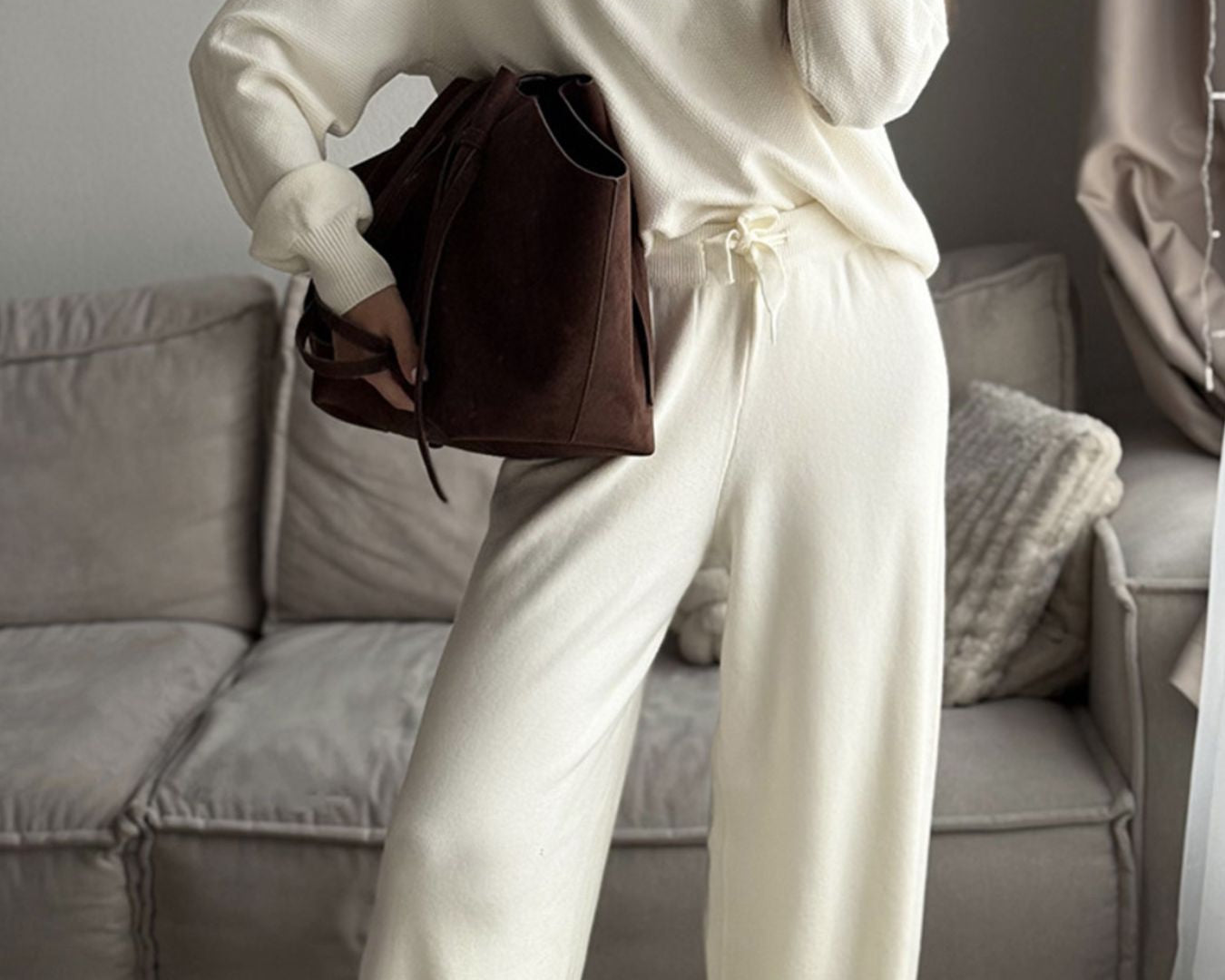 NEWYORKLISTED Comfort Collection: Person wearing a white outfit holding a brown bag in a living room.