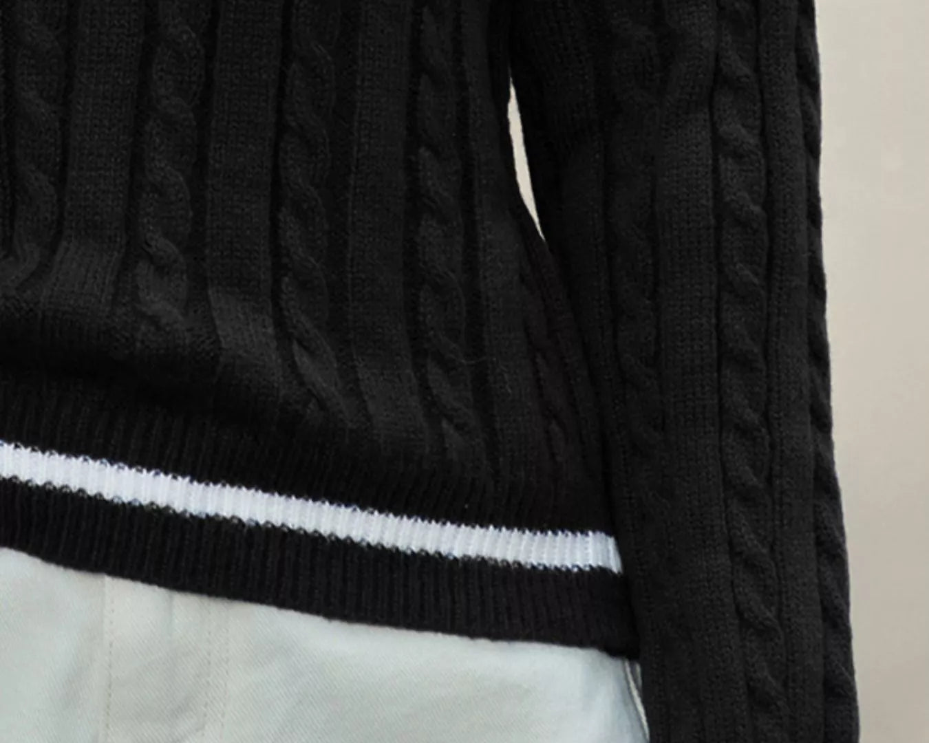 NEWYORKLISTED STYLE COLLECTION: Black cable knit sweater with white trim on a neutral background