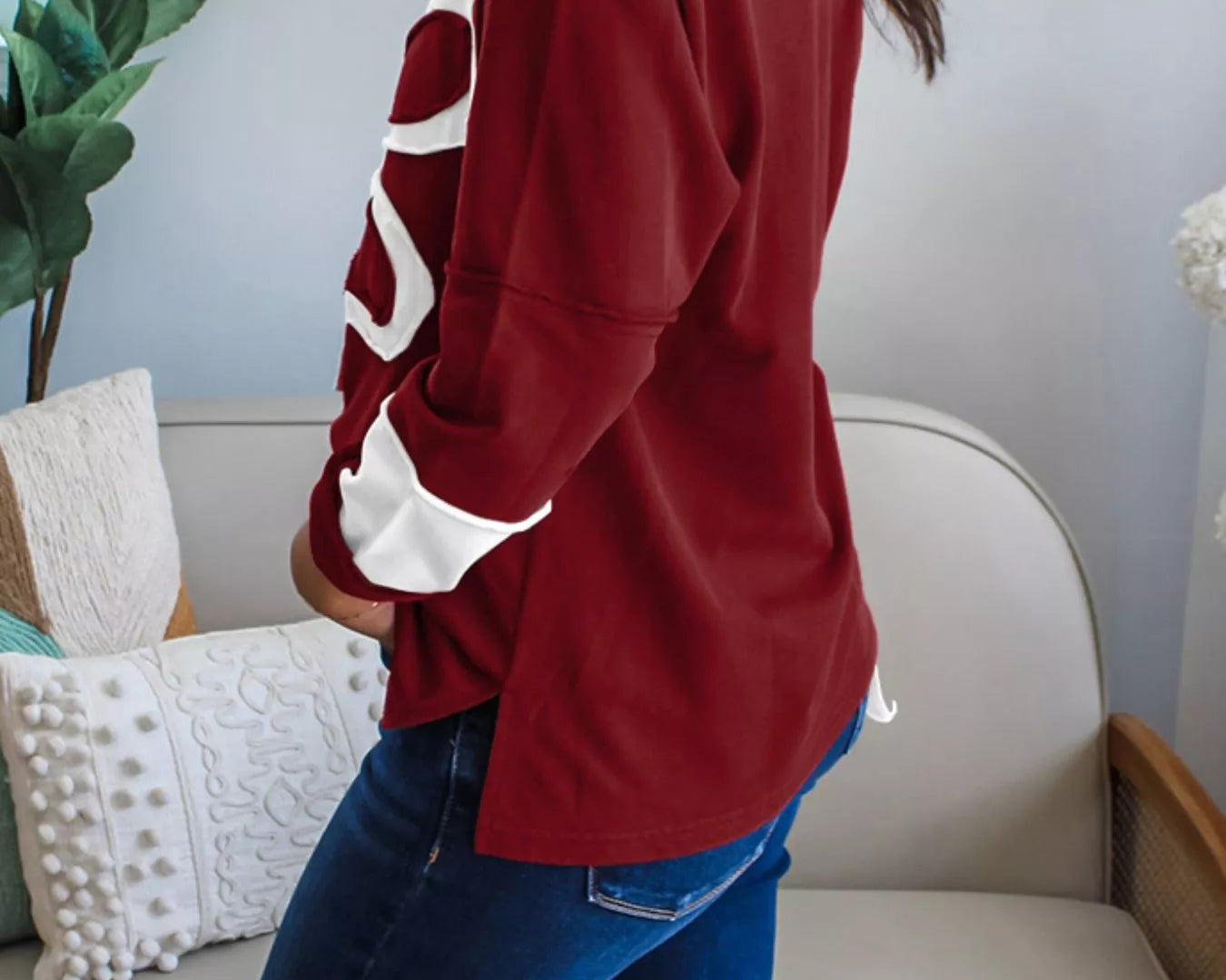 NEWYORKLISTED STYLE COLLECTION: Person wearing a red sweatshirt with white lettering in a living room setting.