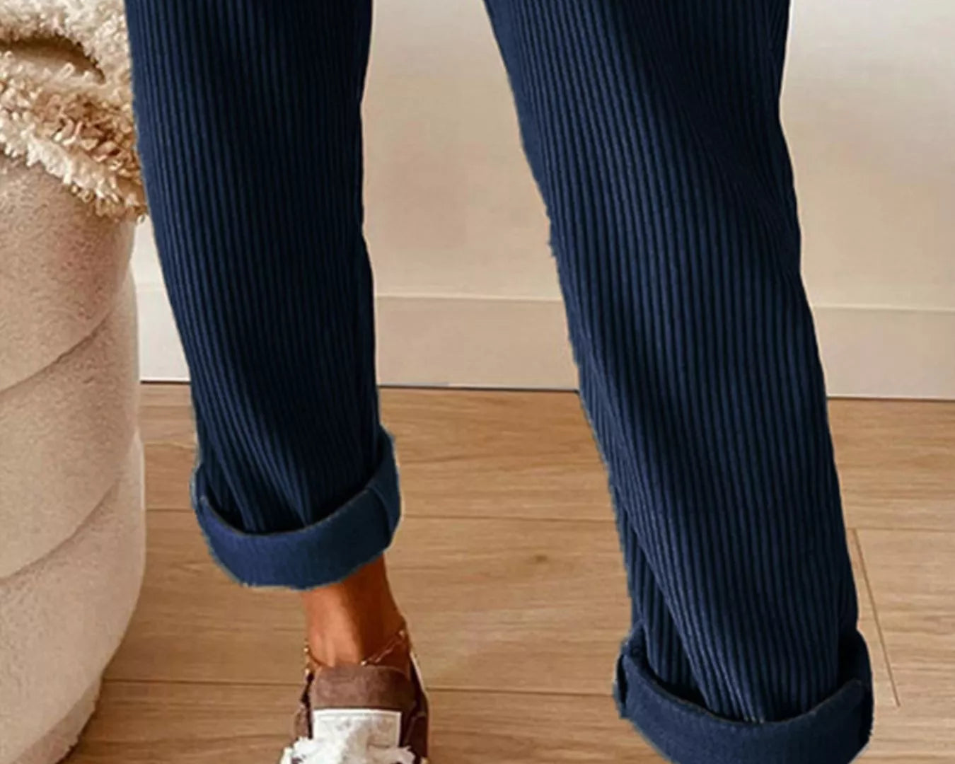 Navy blue ribbed pants with rolled-up cuffs worn with brown loafers on a wooden floor.