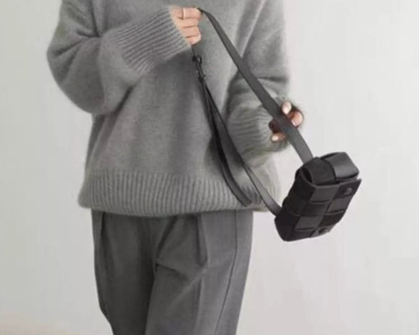Person wearing a gray sweater and pants holding a black bag against a white background