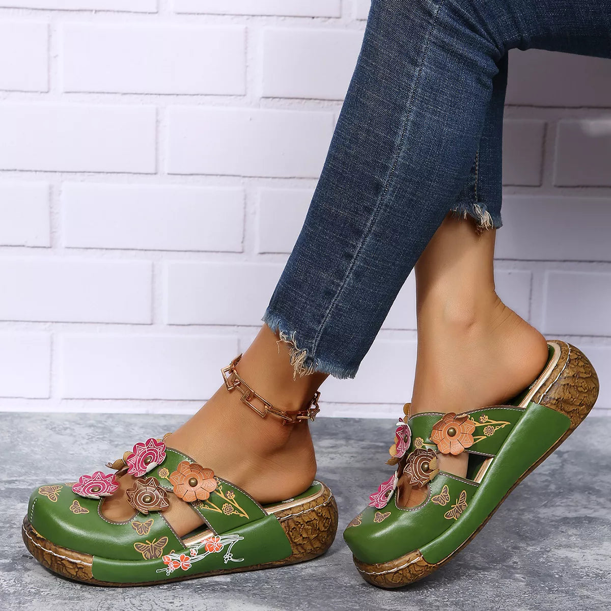 NEWYORKLISTED SHOE COLLECTION: Green sandals with floral designs worn by a person against a white brick wall.