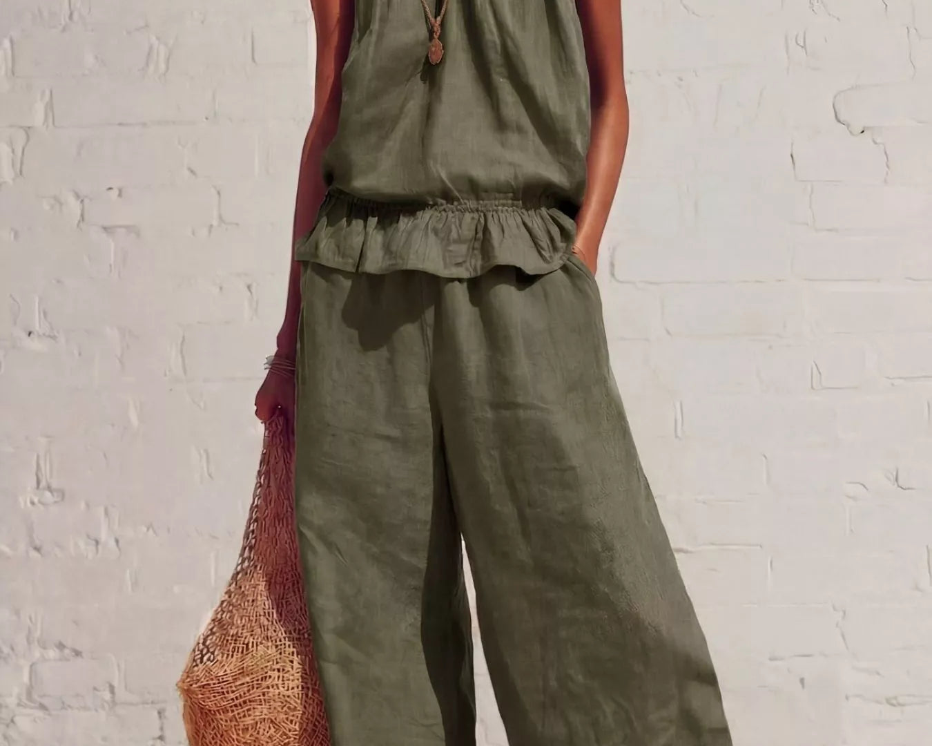 NEWYORKLISTED STYLE COLLECTION: Woman wearing an olive green jumpsuit against a white brick wall.
