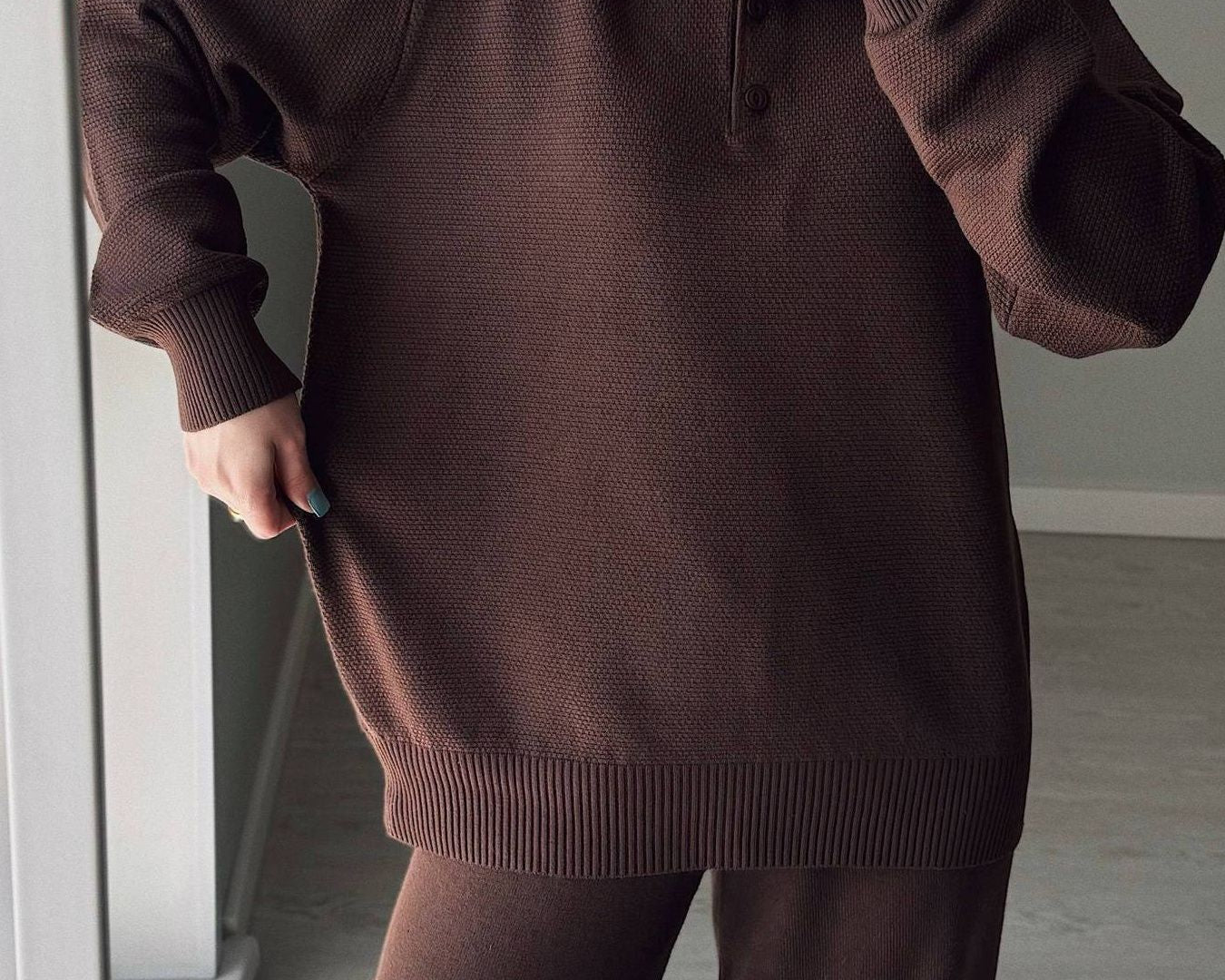 NEWYORKLISTED Comfort Collection: Person wearing a brown sweater and pants in a minimal indoor setting.