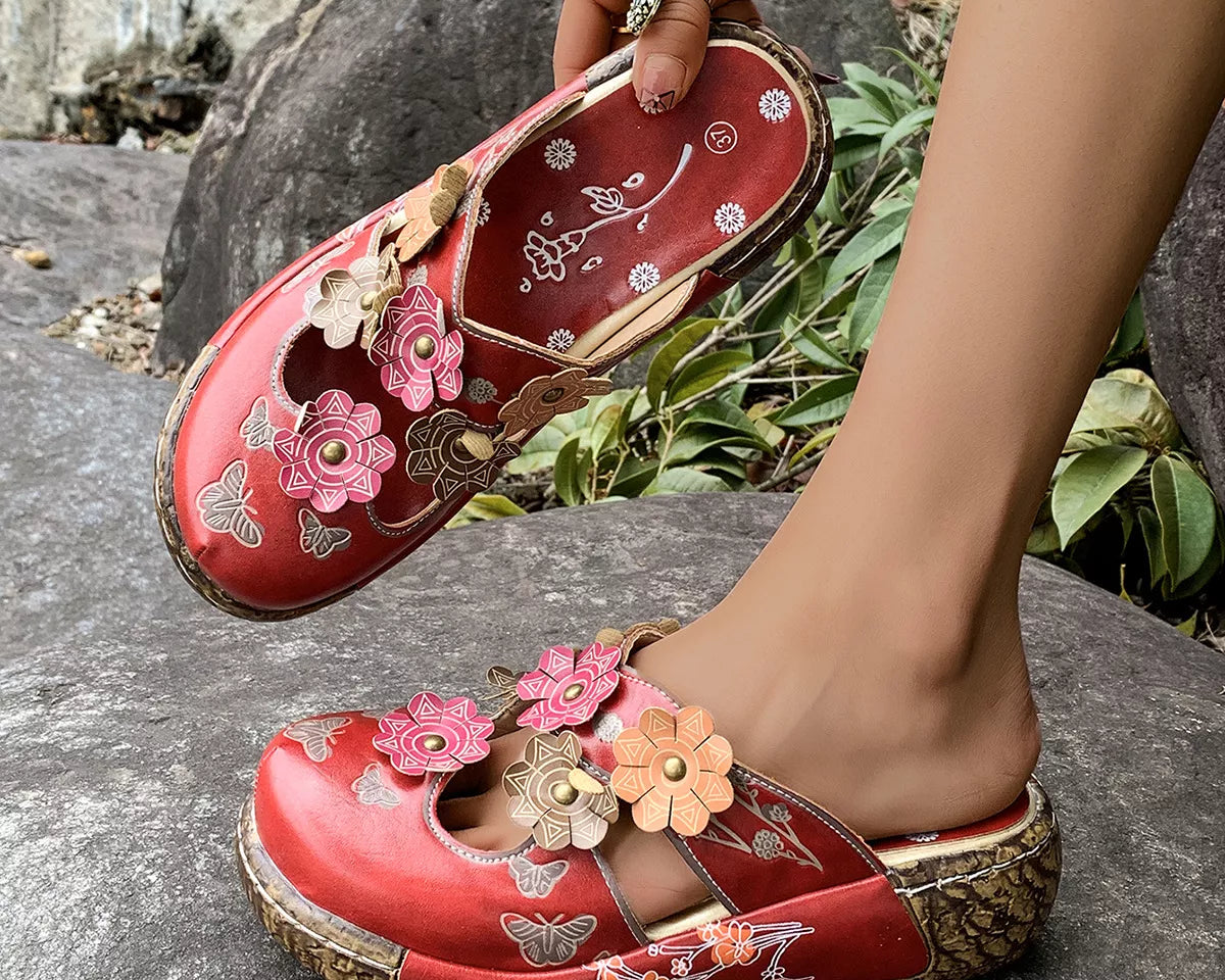 NEWYORKLISTED SHOE COLLECTION: Red floral sandals being worn on a stone surface with greenery in the background