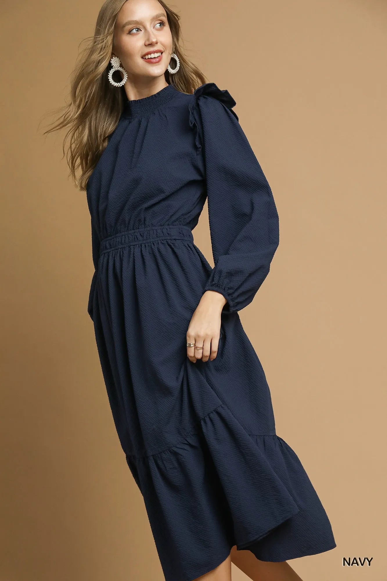 NEWYORKLISTED STYLE COLLECTION: Woman wearing a navy dress against a brown background