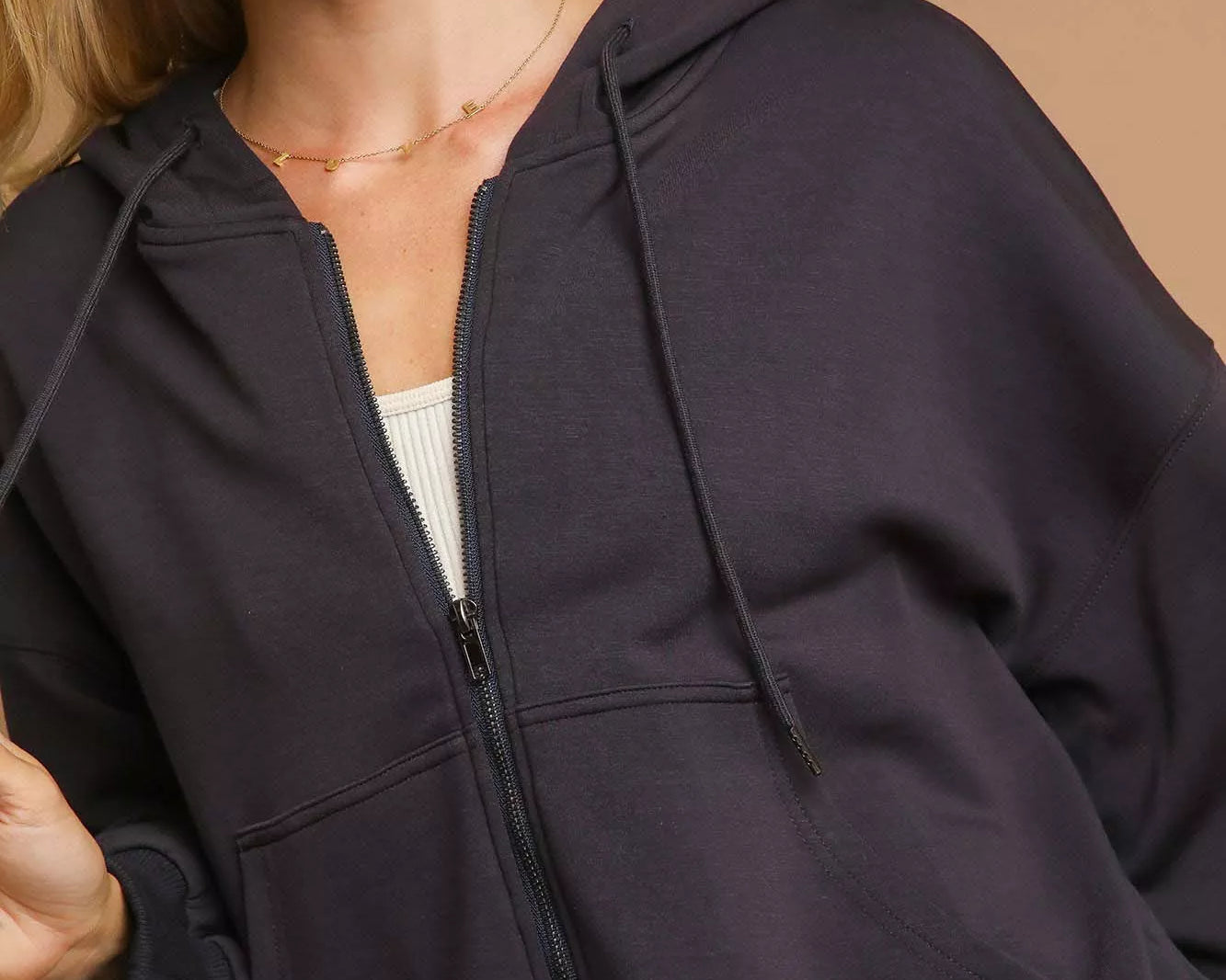 Woman wearing a charcoal gray hoodie against a beige background
