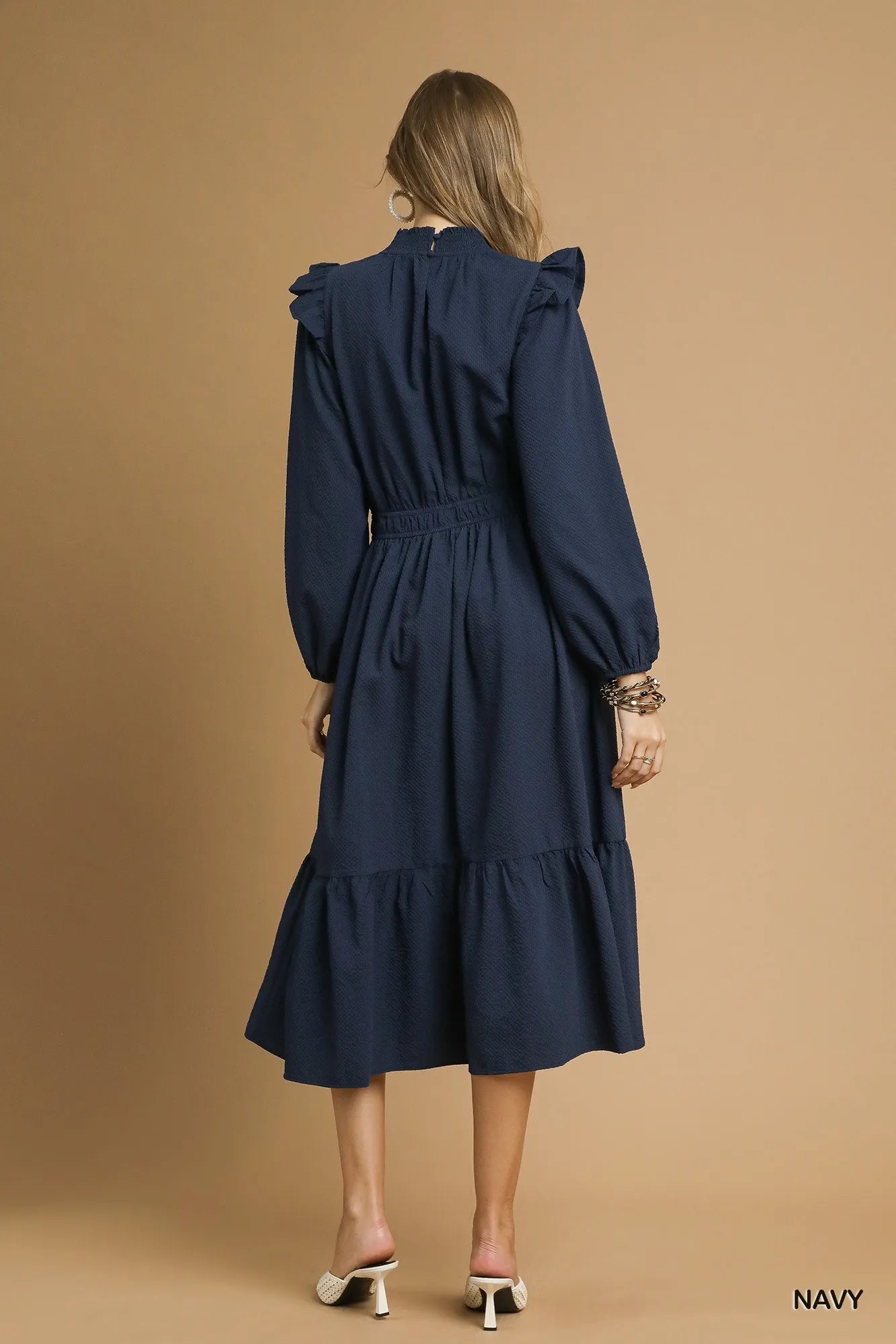 NEWYORKLISTED STYLE COLLECTION: Woman wearing a navy dress against a beige background