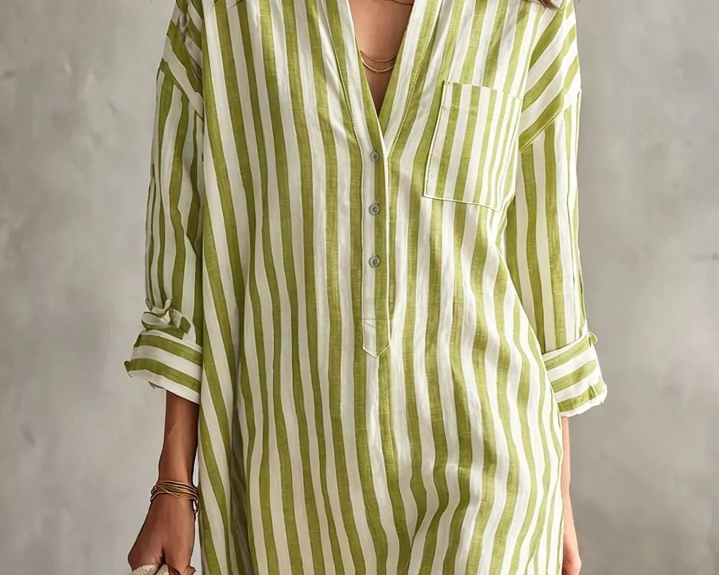 NEWYORKLISTED STYLE COLLECTION: A woman models a light green and white vertically striped linen shirt dress, holding a matching striped tote bag against a textured gray wall.