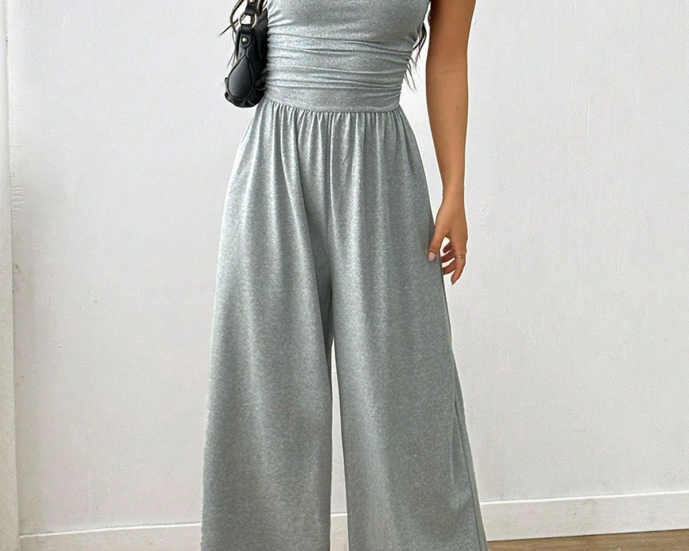 NEWYORKLISTED Comfort Collection: Woman wearing a gray jumpsuit against a white wall.