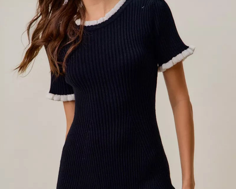 NEWYORKLISTED STYLE COLLECTION: Woman wearing a black dress with white trim on a plain background