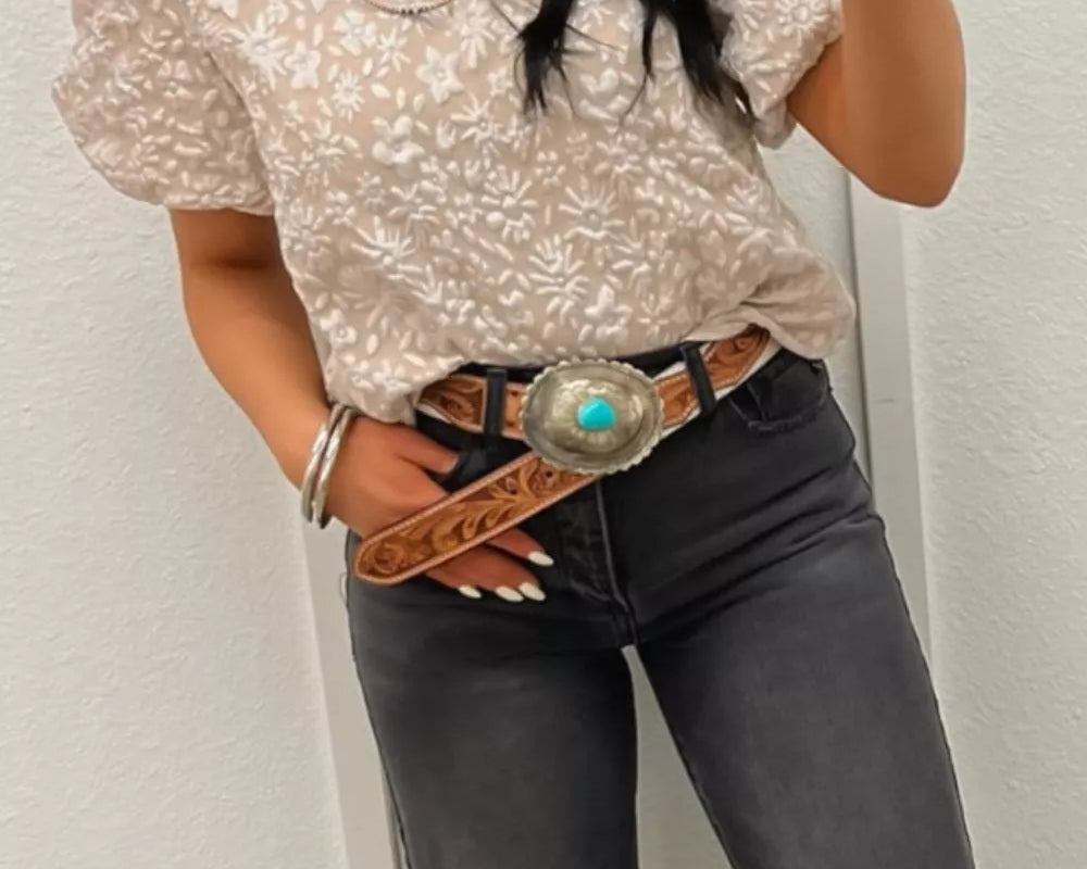 NEWYORKLISTED STYLE COLLECTION: Woman wearing a patterned blouse and black jeans with a belt, taking a mirror selfie.